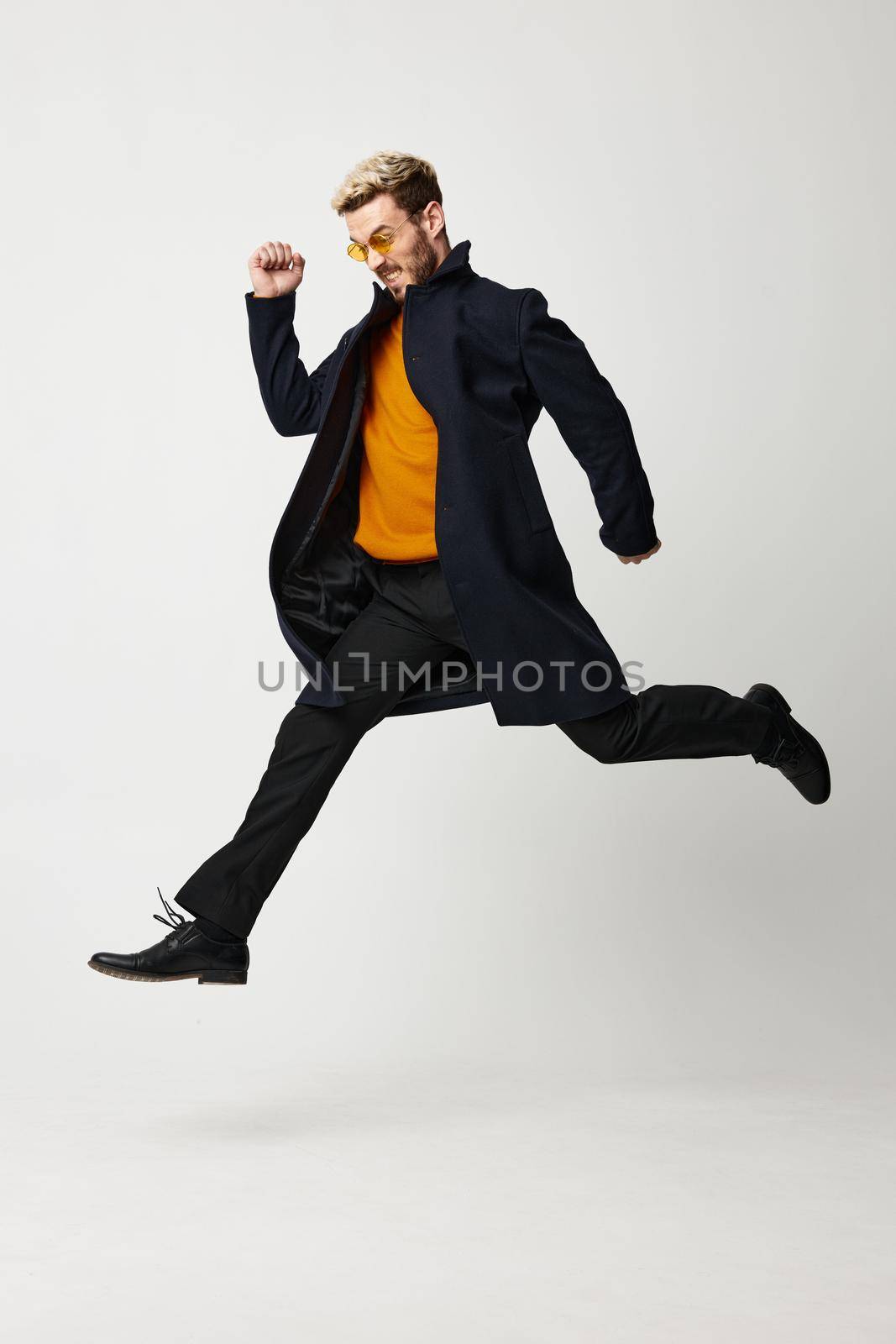 a man jumped and runs to the side on a light background in a coat, trousers and boots. High quality photo