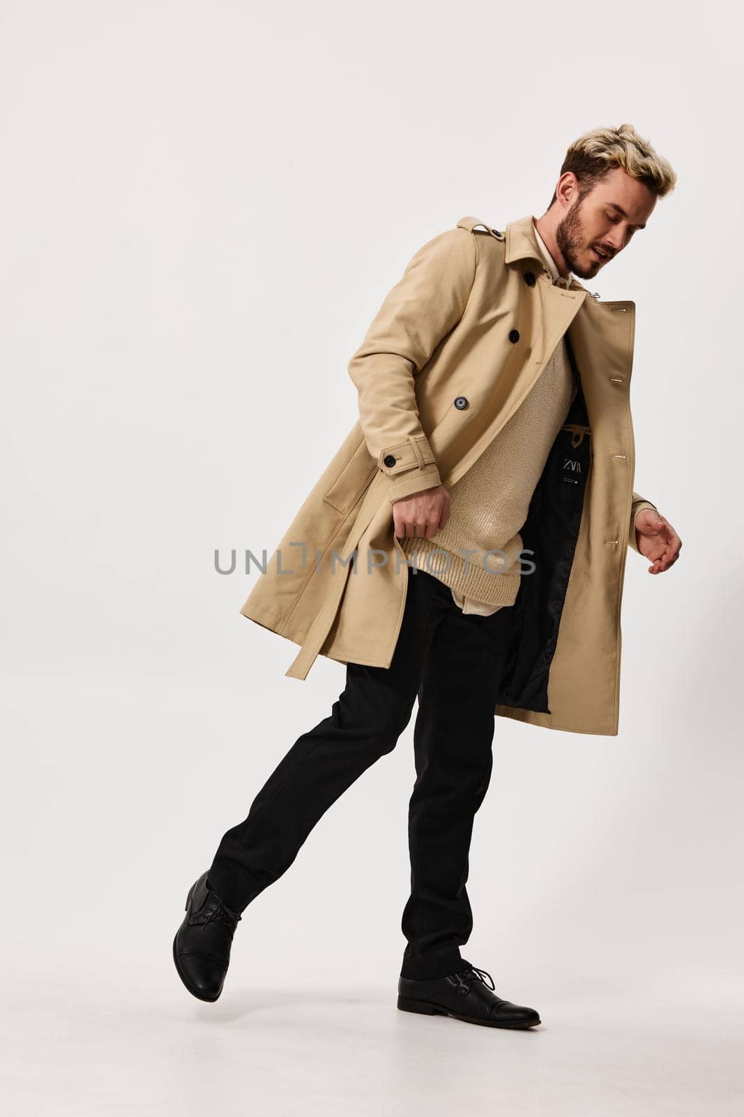 a man in a beige coat, trousers and a sweater bent over to the side on a light background in full growth. High quality photo