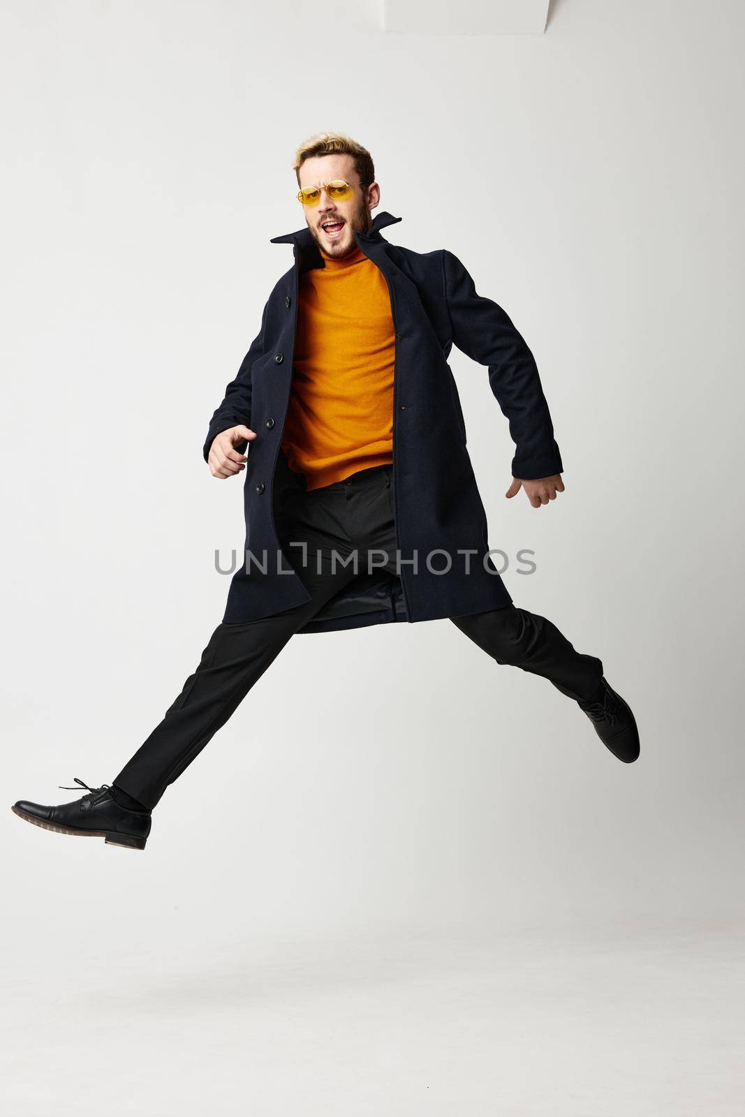 a man with legs wide apart runs forward on a light background and a black coat pants model. High quality photo