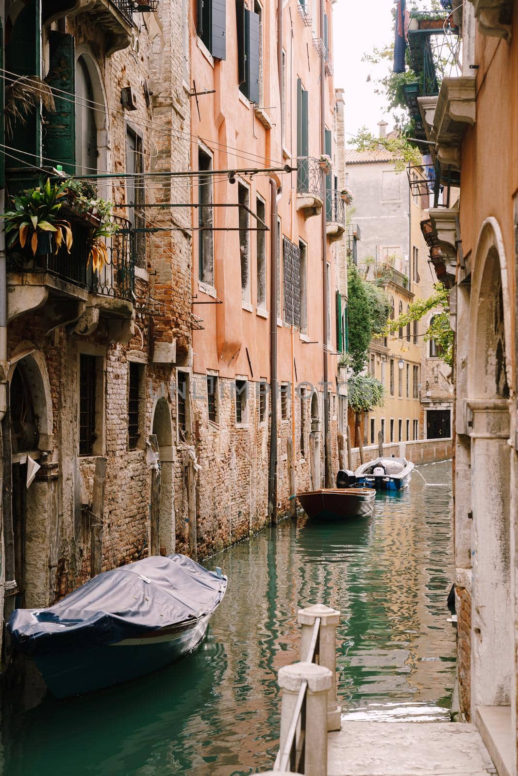 Boats moored at the walls of a building in canal in Venice, Italy. Classic Venetian street views - wooden shutters, brick houses, bridges