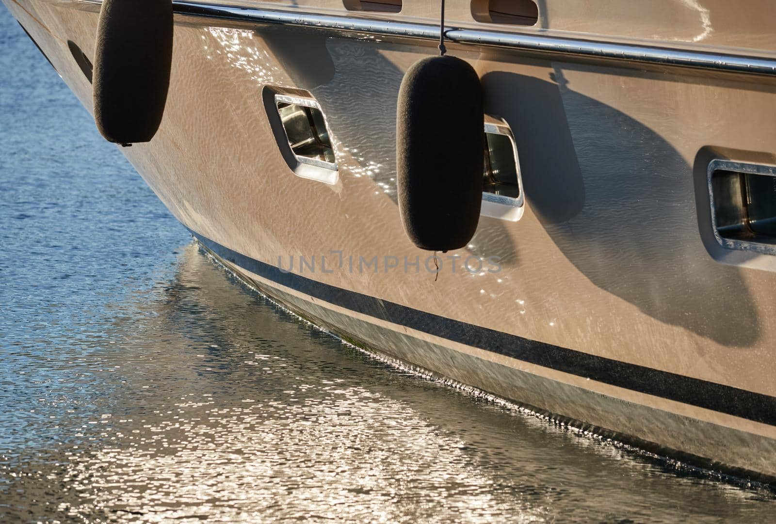 Board of the big boat of gold color, golden reflections of the sun on water at sunset, interesting texture, smooth lines
