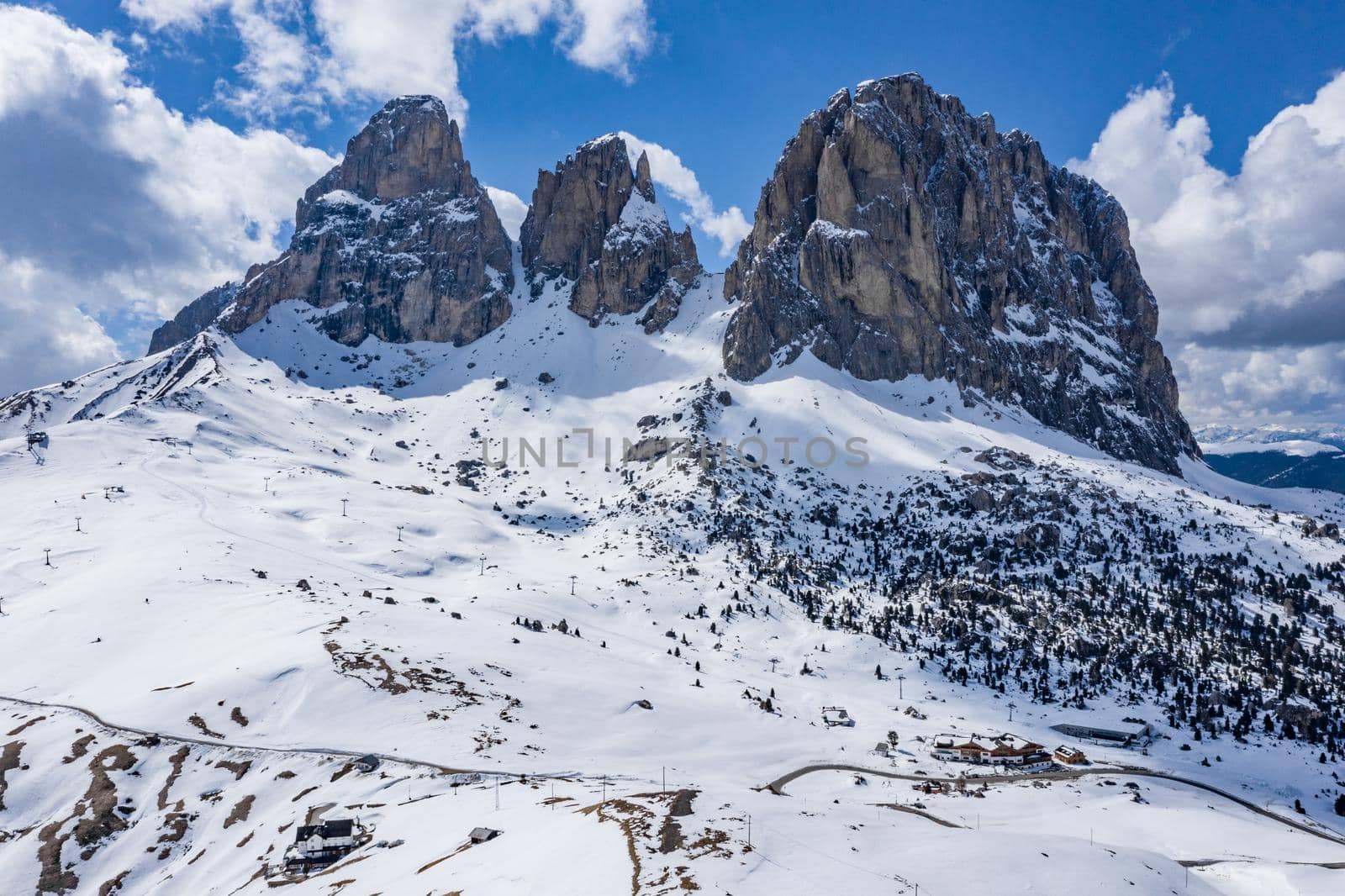 Aerial view of the Dolomites snow-covered mountains in Italy at sunny day, Canazei, drone view point, the twisted road, the blue sky with white clouds, famous place in the world, UNESCO monument by vladimirdrozdin