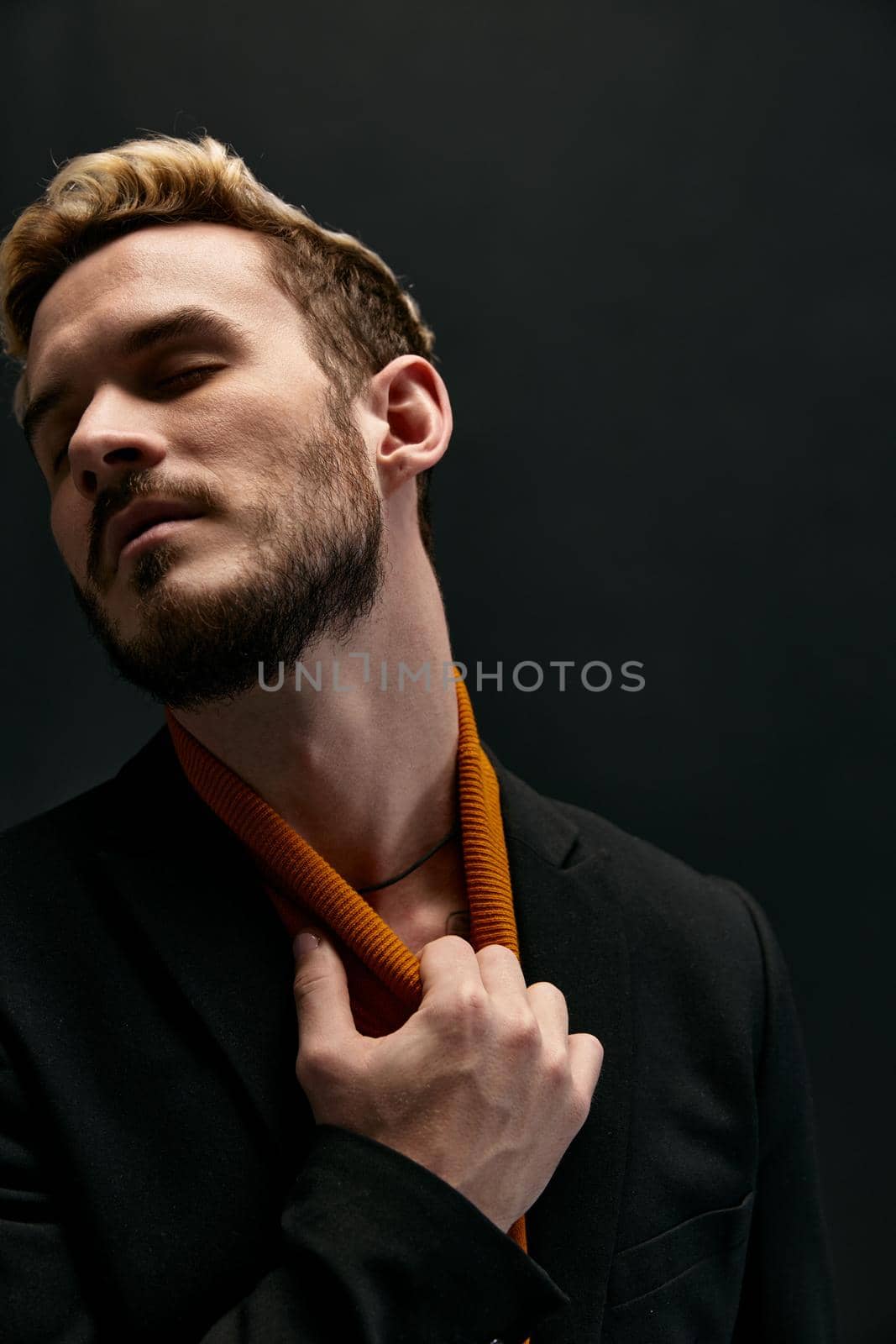 a man touches his neck on a dark background and smiles portrait of a blond . High quality photo