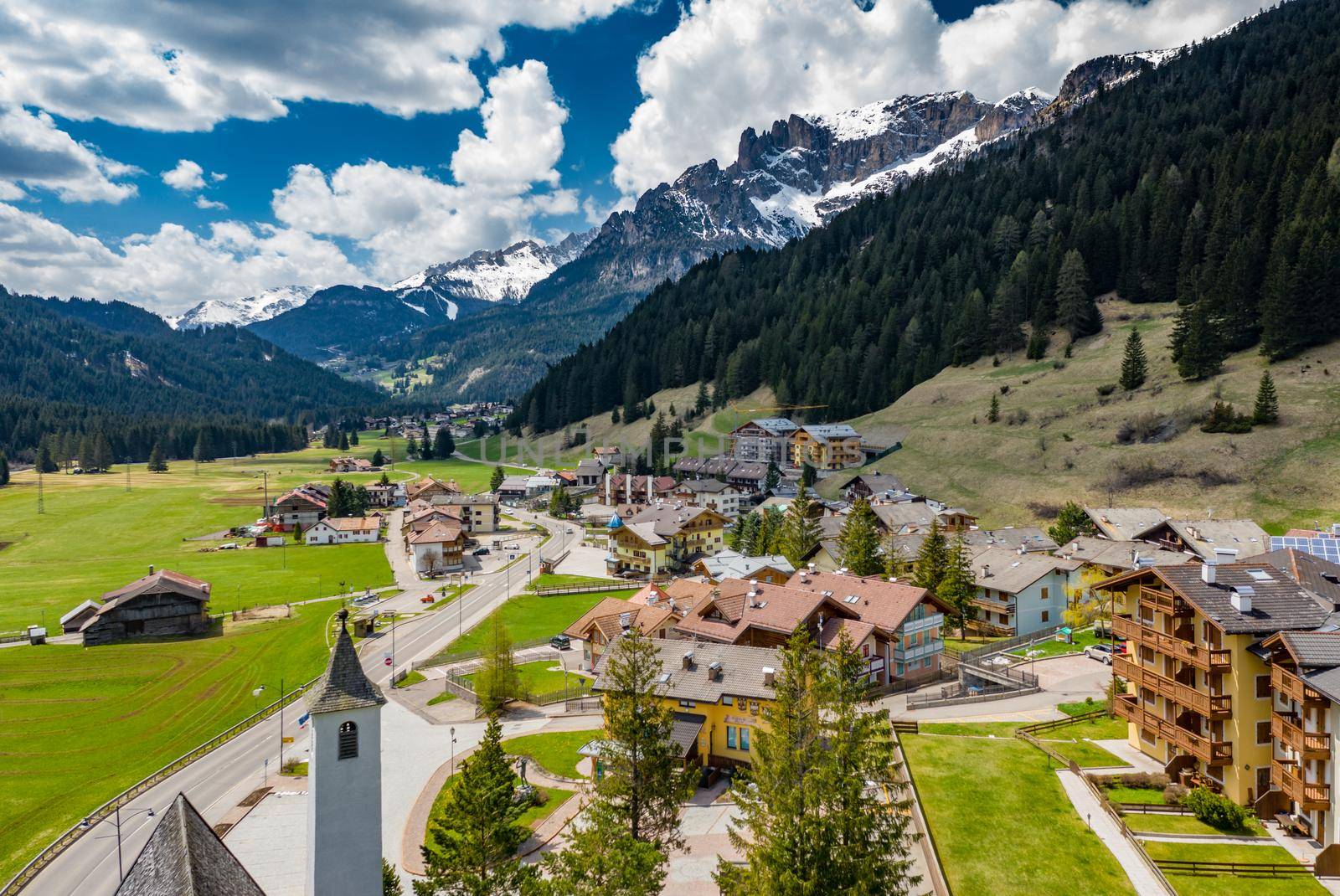 Aerial view of valley with Chalet, green slopes of the mountains of Italy, Trentino, Fontanazzo, huge clouds over a valley, roofs of houses of settlements, green meadows, Dolomites on background, by vladimirdrozdin