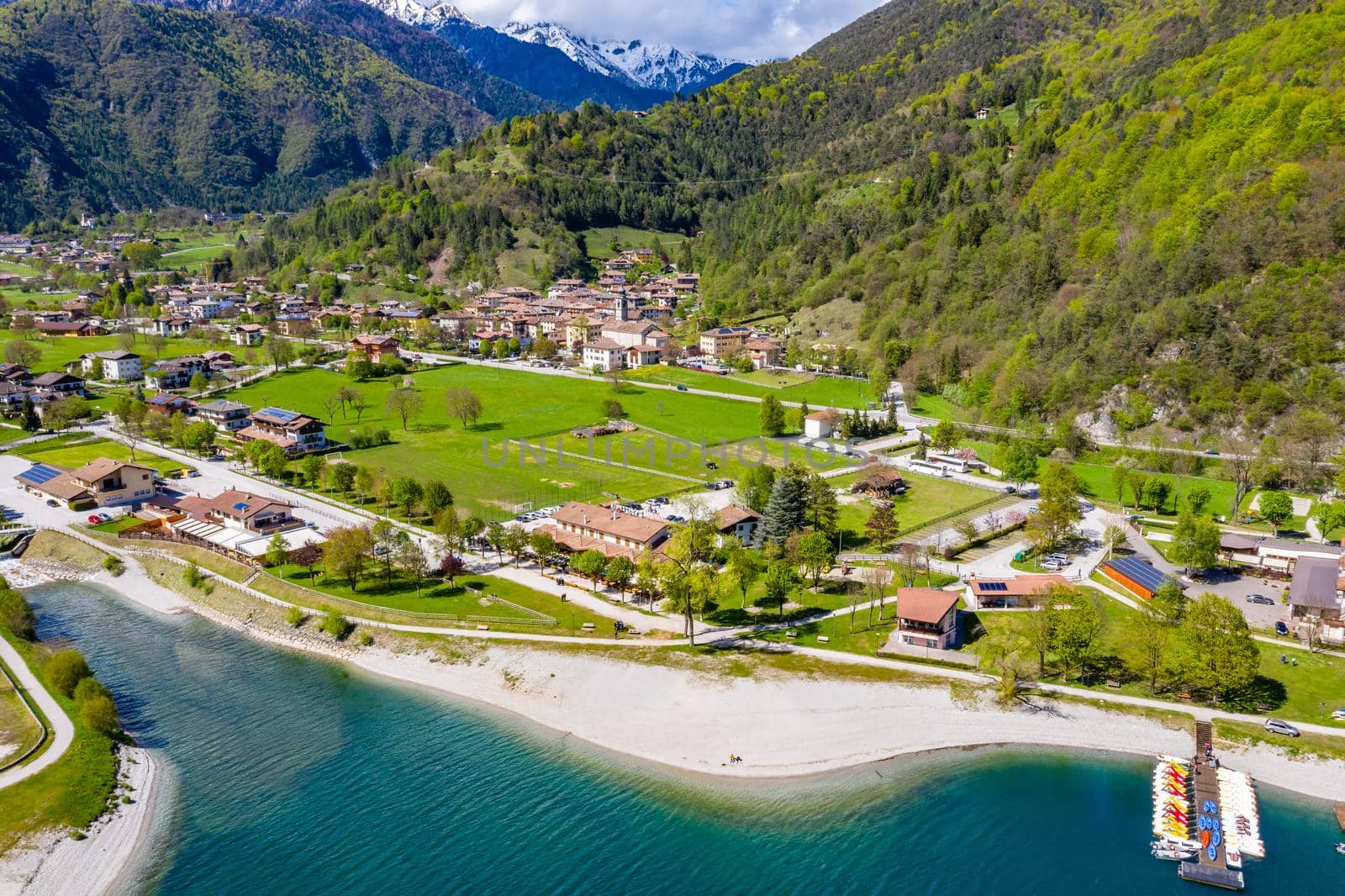 The Improbable aerial landscape of village Molveno, Italy, azure water of lake, empty beach, snow covered mountains Dolomites on background, roof top of chalet, sunny weather, a piers, coastline, slopes