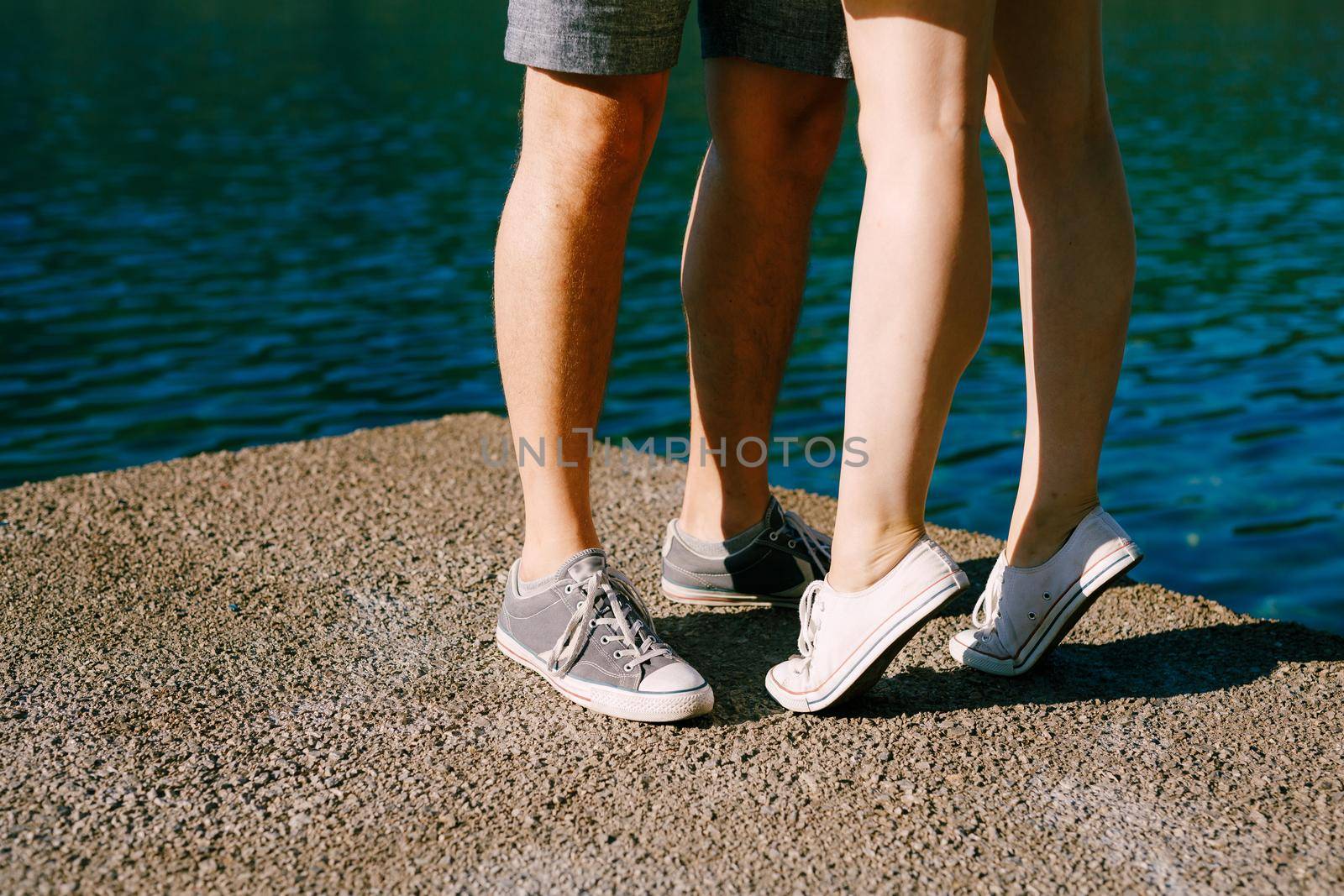 Legs of a man and a woman in sneakers standing hugging each other on the pier close-up, a woman is standing on tiptoe . High quality photo