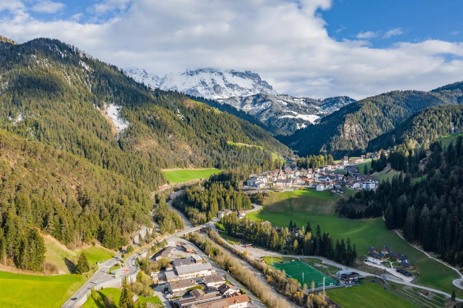 Aerial view of improbable green meadows of Italian Alps, Comano Terme, huge clouds over a valley, roof tops of houses, Dolomites on background, sunshines through clouds by vladimirdrozdin