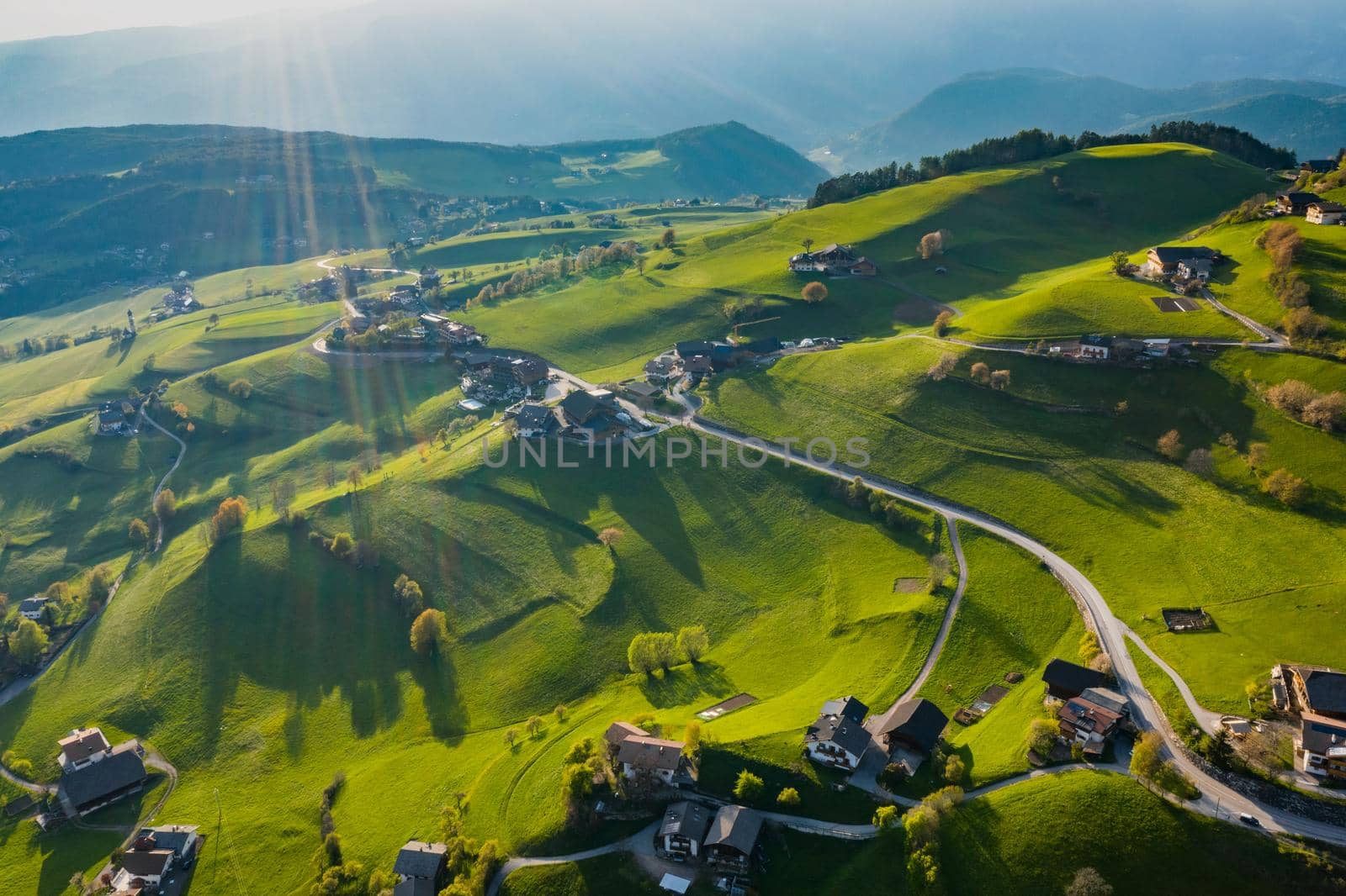 Aerial view of improbable green meadows of Italian Alps, green slopes of the mountains, Bolzano, huge clouds over a valley, roof tops of houses, Dolomites on background, sunshines through clouds by vladimirdrozdin