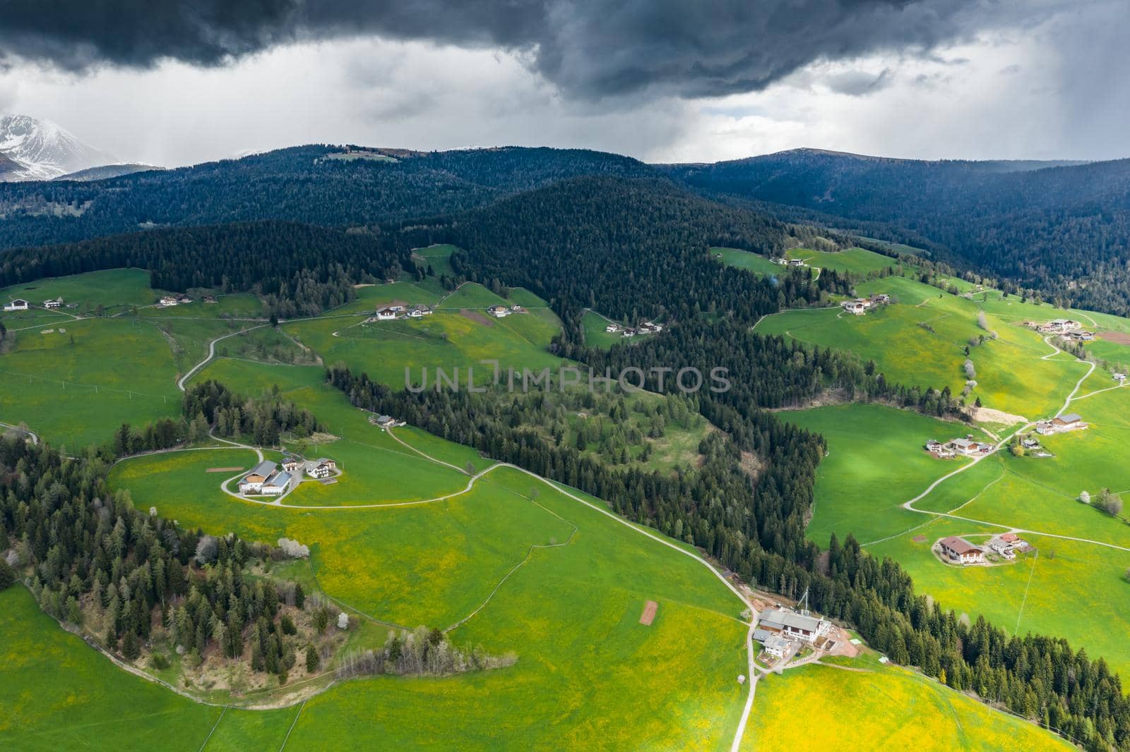 Aerial view of improbable green meadows of the Italian Alps, green slopes of the mountains, Bolzano, huge clouds over a valley, roof tops of houses, Dolomites on background, sunshines through clouds