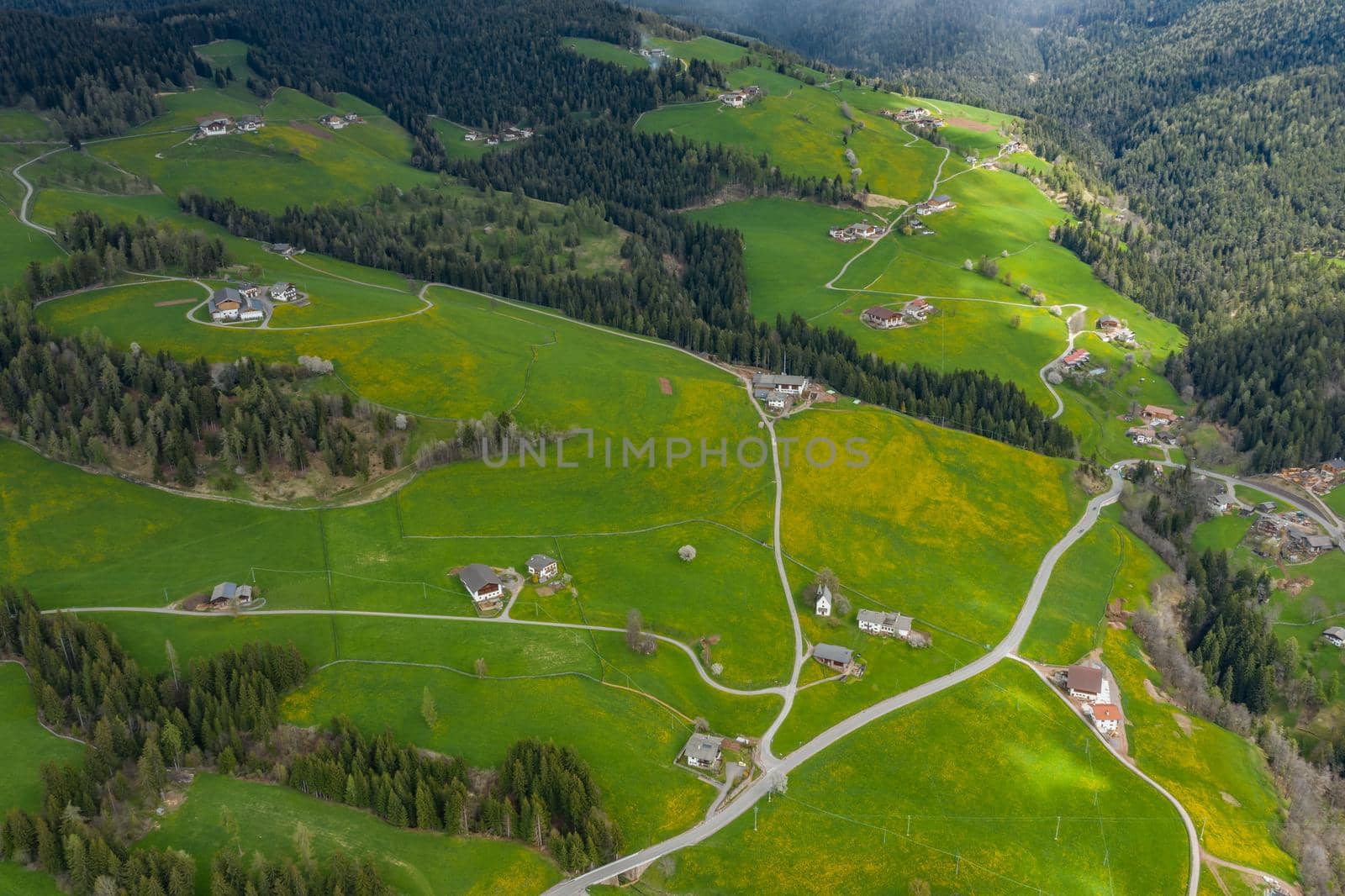 Aerial view of improbable green meadows of Italian Alps, green slopes of the mountains, Bolzano, huge clouds over a valley, roof tops of houses, Dolomites on background, sunshines through clouds by vladimirdrozdin