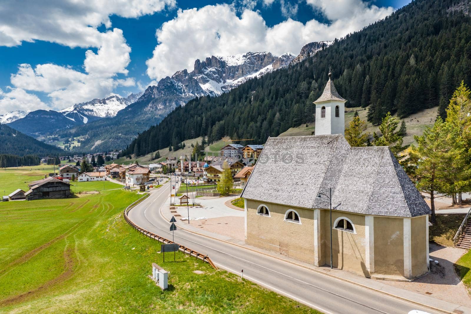 Aerial view of valley with Chalet, green slopes of the mountains of Italy, Trentino, Fontanazzo, huge clouds over a valley, roofs of houses of settlements, green meadows, Dolomites on background, sunny weather