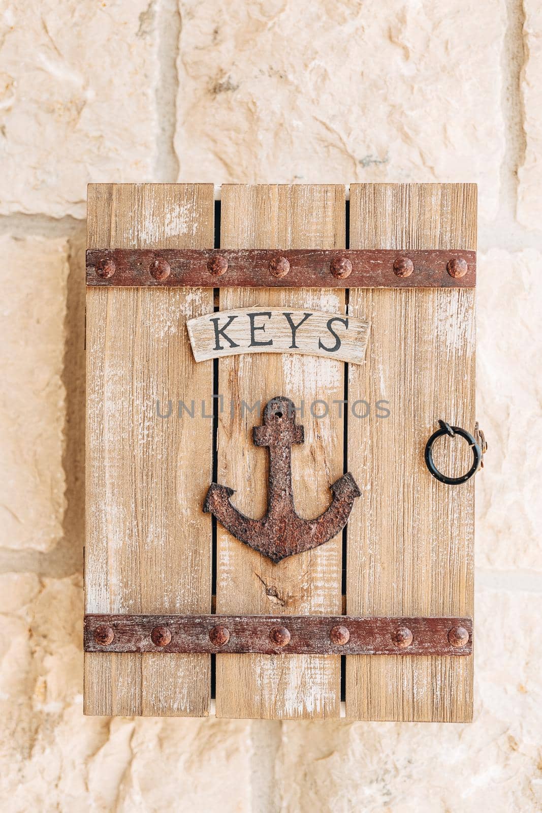 A wooden key box with the inscription Keys and a metal ship anchor hangs on a stone wall