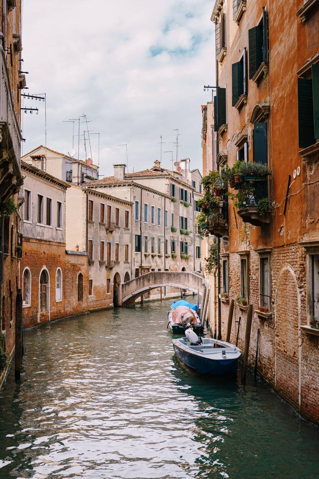 Boats moored at the walls of a building in canal in Venice, Italy. Classic Venetian street views - wooden shutters, brick houses, bridges