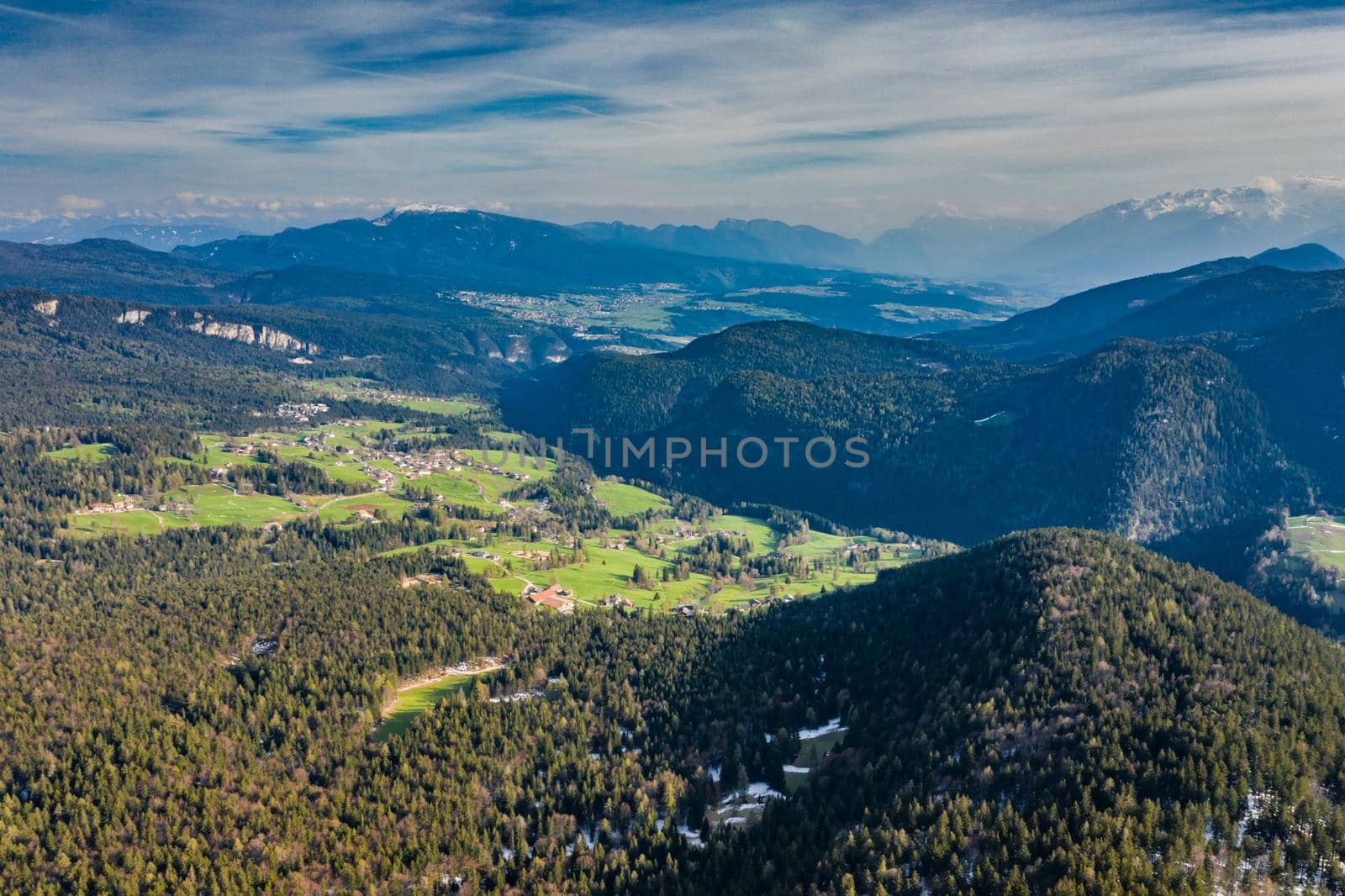 Aerial view of huge valley of the mountains of Italy, Trentino, Slopes with green spruce trees, Dolomites on background, The town in the bottom of a valley