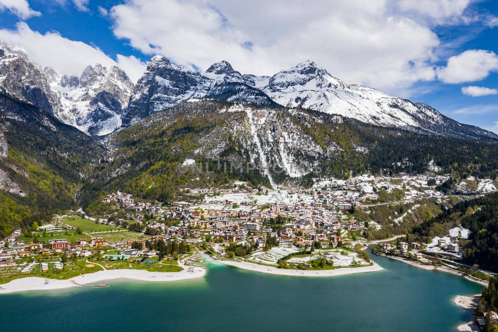 The Improbable aerial landscape of village Molveno, Italy, azure water of lake, empty beach, snow covered mountains Dolomites on background, roof top of chalet, sunny weather, a piers, coastline, by vladimirdrozdin