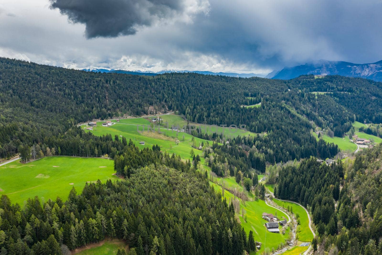 Aerial view of improbable green meadows of the Italian Alps, green slopes of the mountains, Bolzano, huge clouds over a valley, roof tops of houses, Dolomites on background, sunshines through clouds