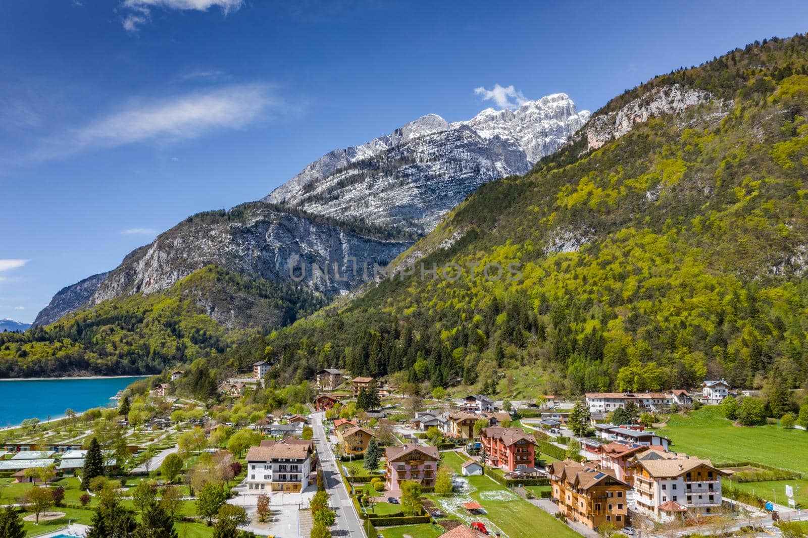 The Improbable aerial landscape of village Molveno, Italy, azure water of lake, empty beach, snow covered mountains Dolomites on background, roof top of chalet, sunny weather, a piers, coastline, slopes