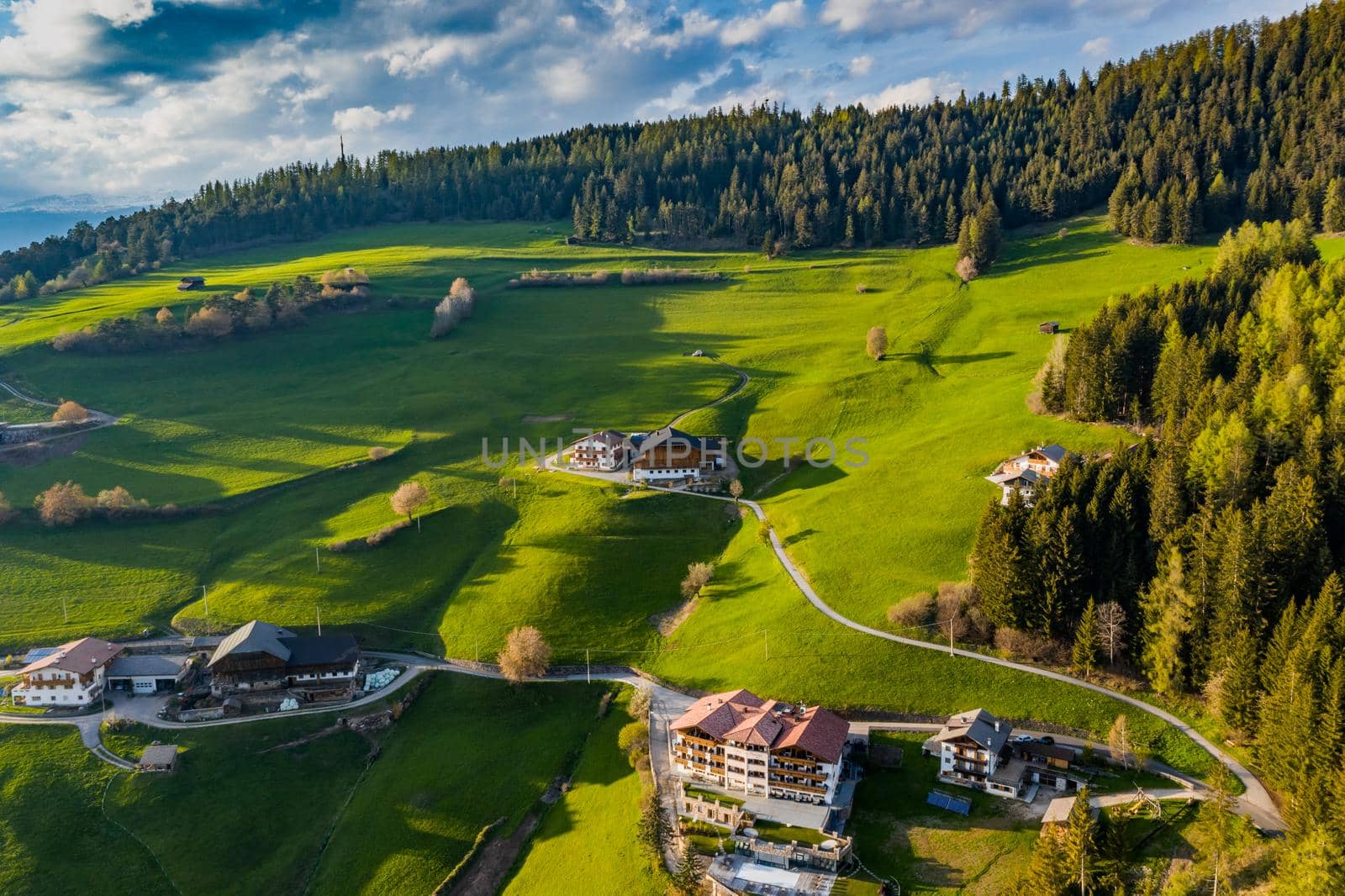 Aerial view of improbable green meadows of Italian Alps, green slopes of the mountains, Bolzano, huge clouds over a valley, roof tops of houses, Dolomites on background, sunshines through clouds by vladimirdrozdin