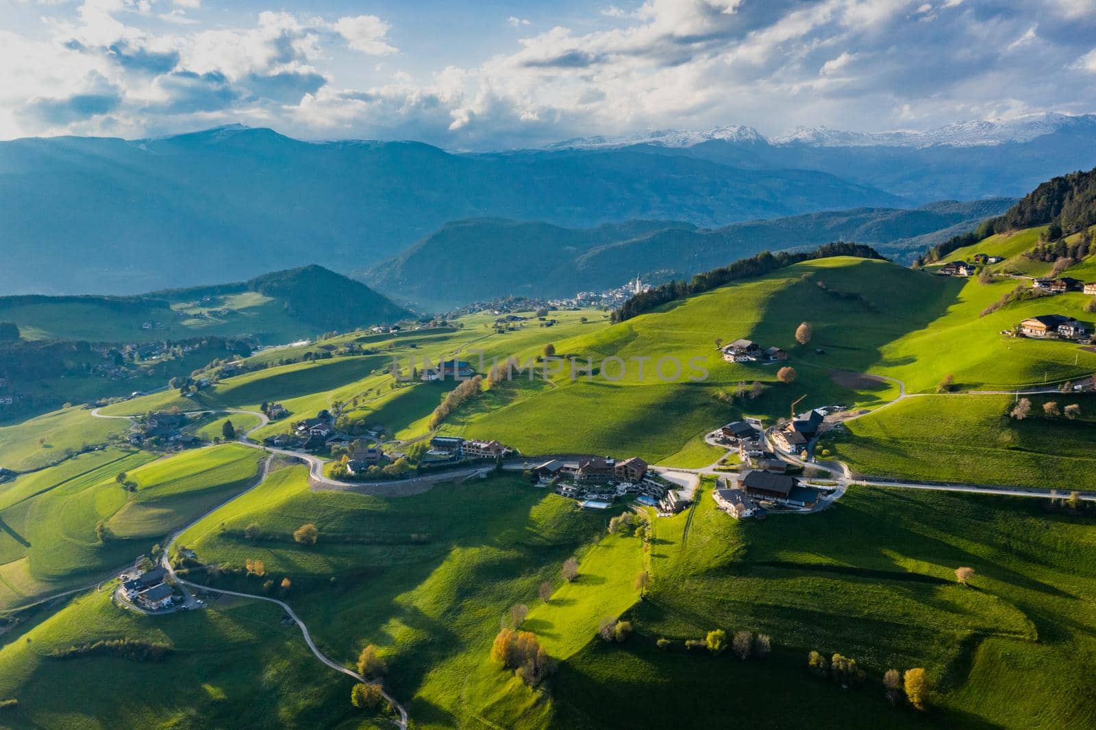 Aerial view of improbable green meadows of Italian Alps, green slopes of the mountains, Bolzano, huge clouds over a valley, roof tops of houses, Dolomites on background, sunshines through clouds by vladimirdrozdin