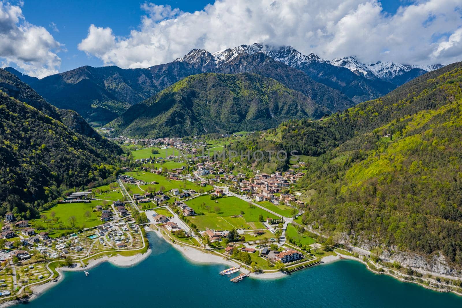 The Improbable aerial landscape of village Molveno, Italy, azure water of lake, empty beach, snow covered mountains Dolomites on background, roof top of chalet, sunny weather, a piers, coastline, slopes