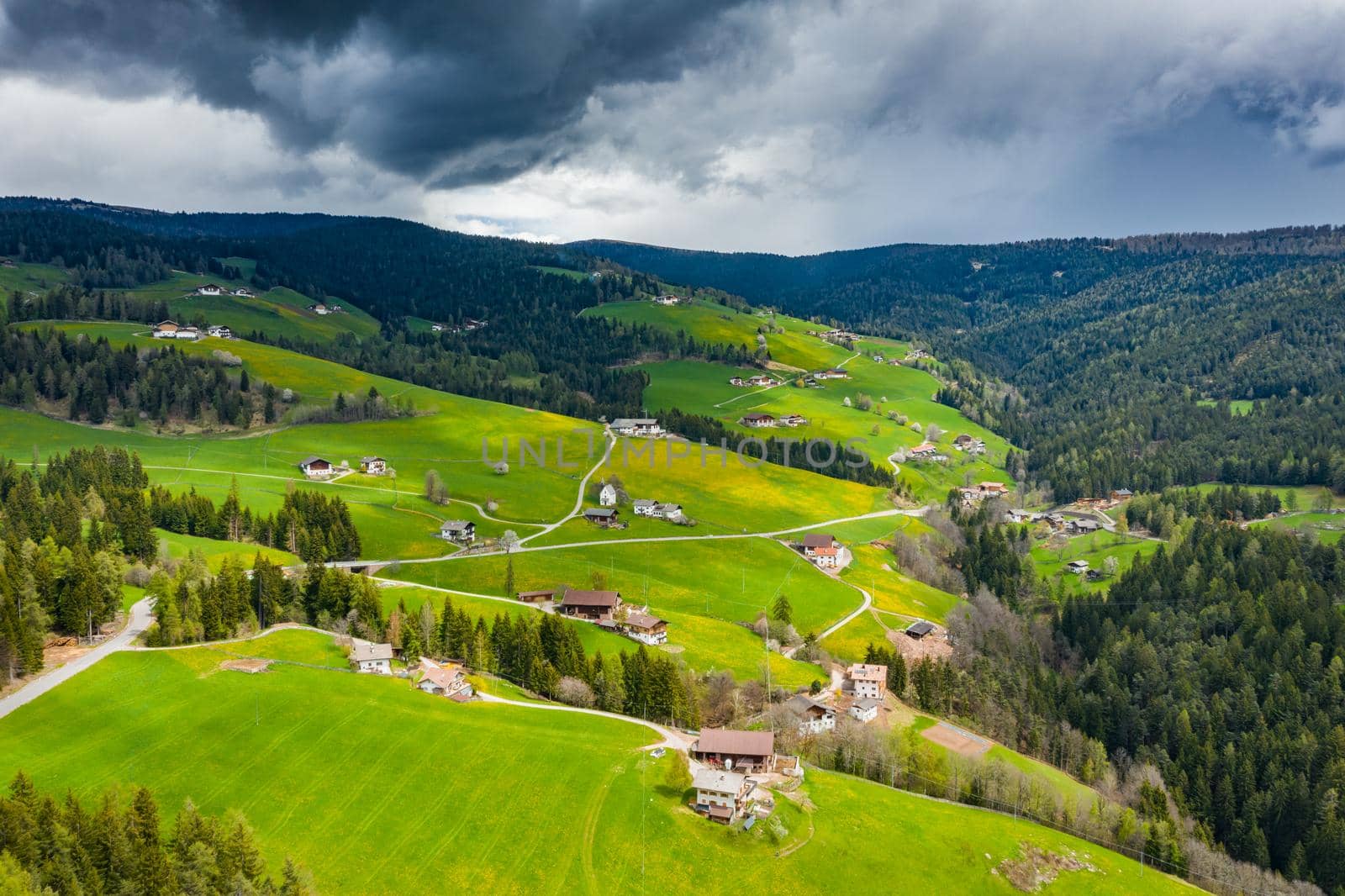 Aerial view of improbable green meadows of Italian Alps, green slopes of the mountains, Bolzano, huge clouds over a valley, roof tops of houses, Dolomites on background, sunshines through clouds by vladimirdrozdin