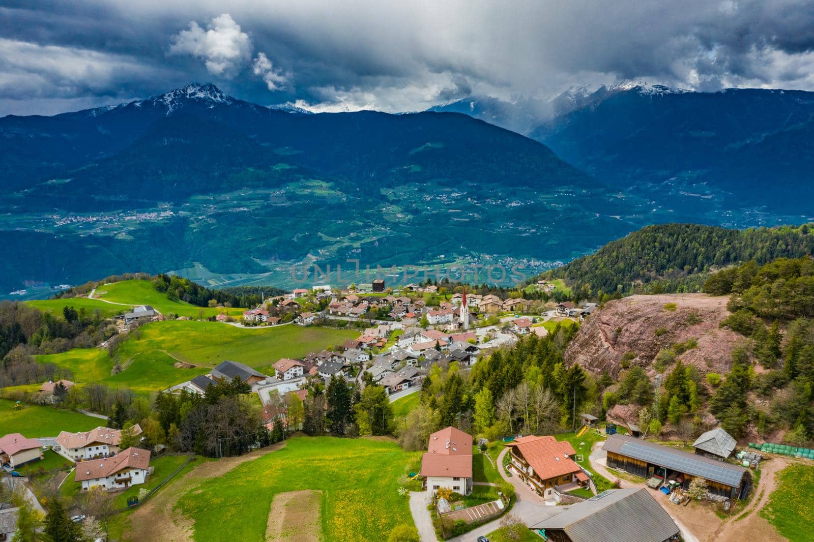 Aerial view of farm of solar batteries on roof top, green slopes of the mountains of Italy, Trentino, huge clouds over a valley, green meadows, a clear energy, energy of the sun, picturesque landscape