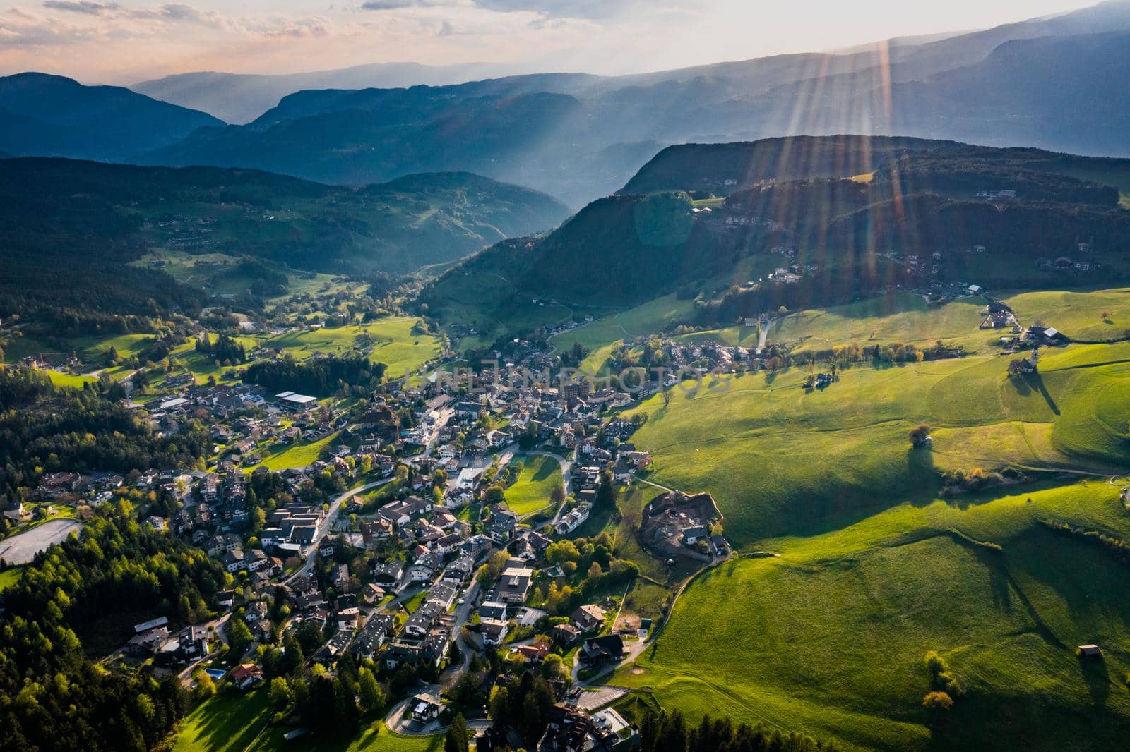 Aerial view of improbable green meadows of Italian Alps, green slopes of the mountains, Bolzano, huge clouds over a valley, roof tops of houses, Dolomites on background, sunshines through clouds by vladimirdrozdin