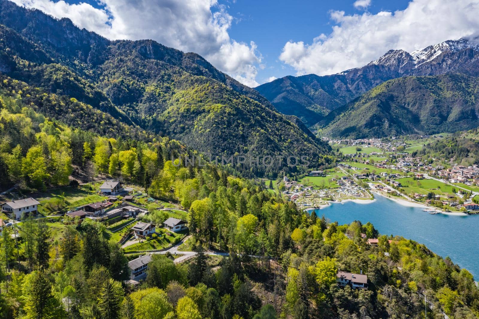 The Improbable aerial landscape of village Molveno, Italy, azure water of lake, empty beach, snow covered mountains Dolomites on background, roof top of chalet, sunny weather, a piers, coastline, slopes