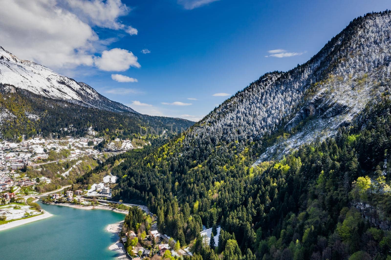 The Improbable aerial landscape of village Molveno, Italy, azure water of lake, empty beach, snow covered mountains Dolomites on background, roof top of chalet, sunny weather, a piers, coastline, by vladimirdrozdin