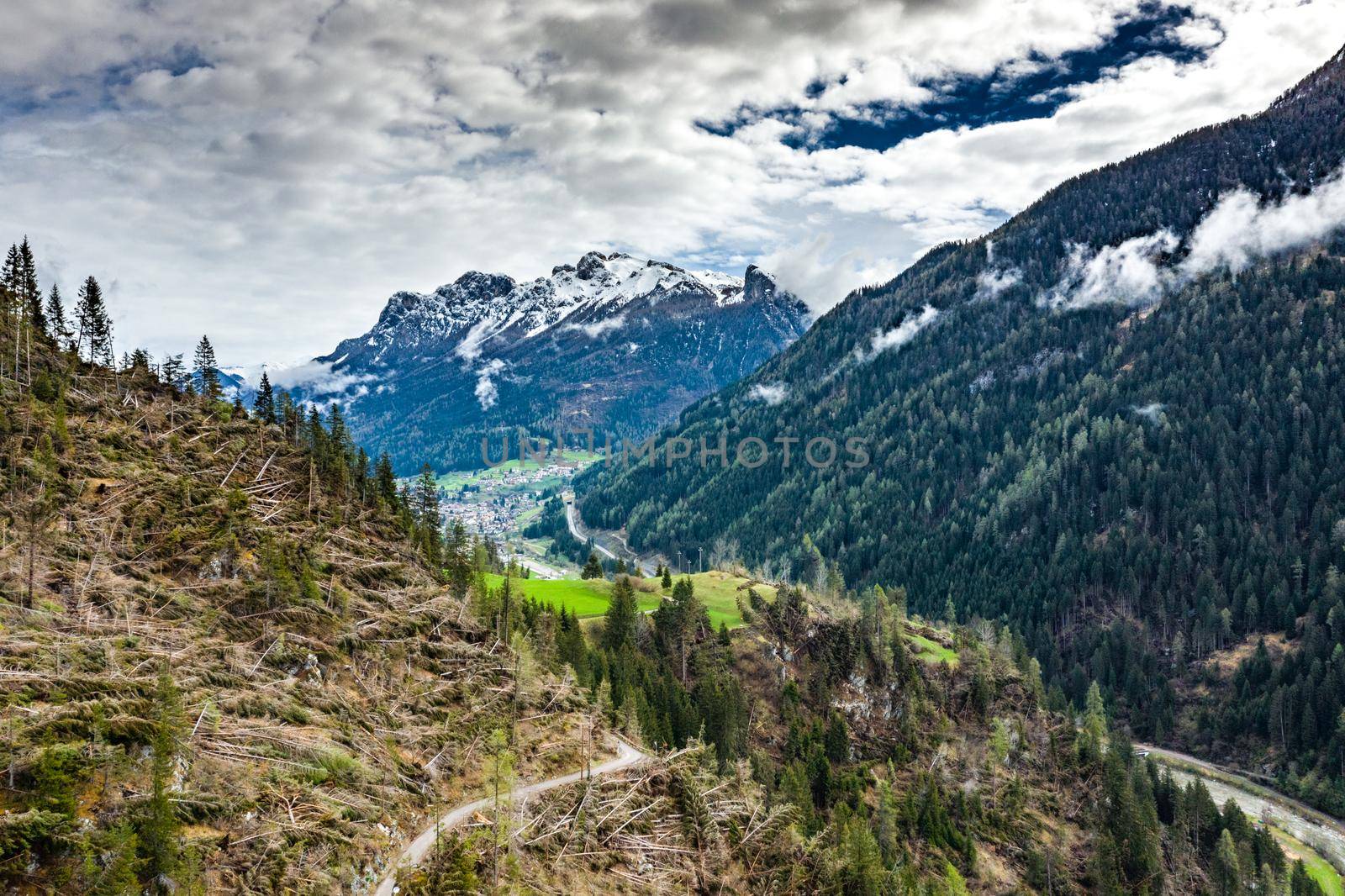 Aerial view of valley with green slopes of the mountains of Italy, Trentino, The trees tumbled down by a wind, huge clouds over a valley, green meadows, Dolomites on background