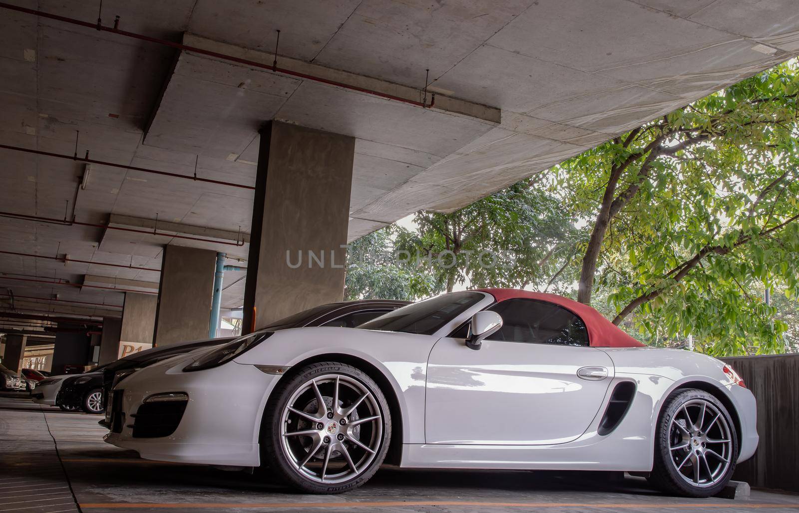 The side of Wheel of White Porsche Sports Car parked in the parking lot.  by tosirikul