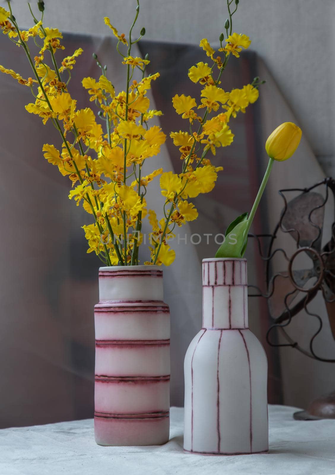 Bouquet of yellow flowers in Two handmade ceramic vase and Vintage fan on white textured table cloth with old cement wall. Home decor, Selective focus.