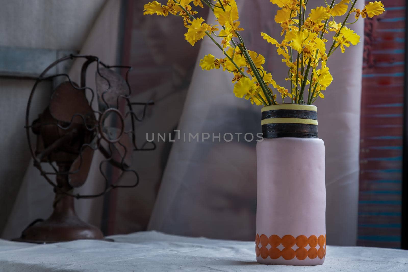 Bouquet of yellow flowers in Handmade ceramic vase and Vintage fan on white textured table cloth with old cement wall. Home decor, Selective focus.