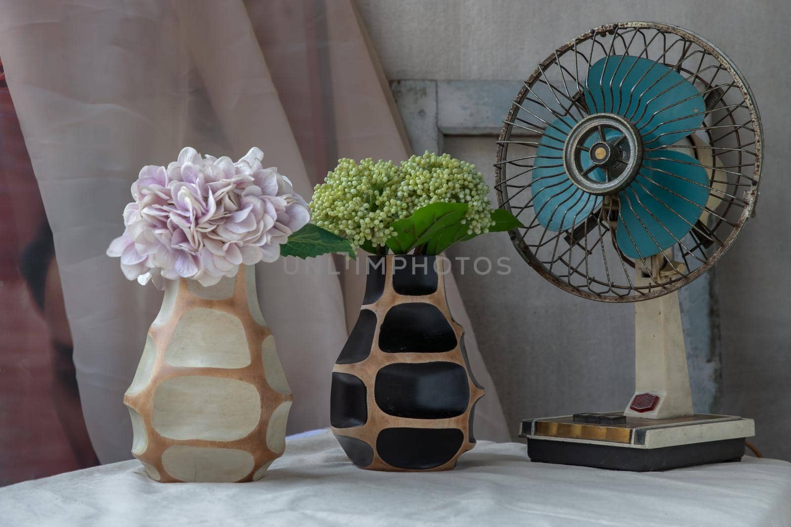 Bouquet of green and purple in Two handmade wooden vase and Vintage fan on white textured table cloth with old cement wall. Home decor, Selective focus.