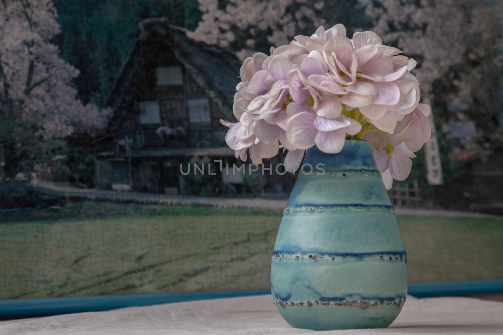Bangkok, Thailand - Feb 06, 2021 : Bouquet of purple flowers in Blue handmade ceramic vase on white textured table cloth in front of Beautiful scenery wallpaper. Home decor, Selective focus.