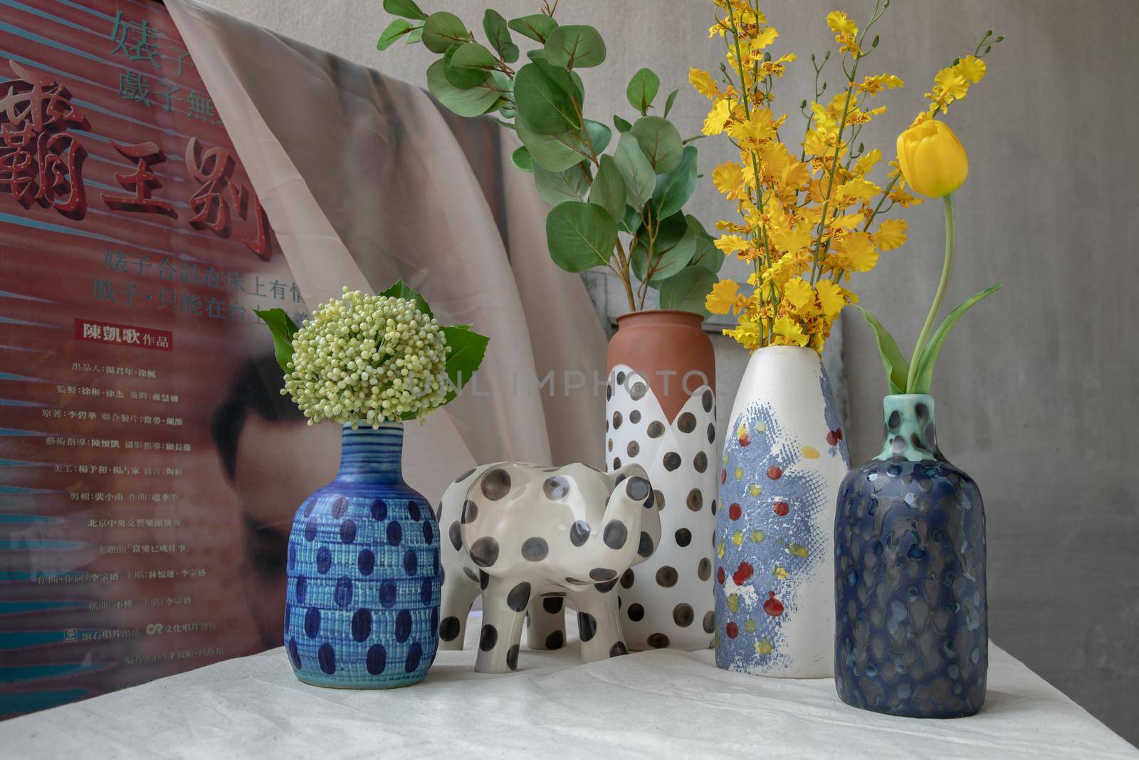Bangkok, Thailand - Feb 06, 2021: Bouquet of many flowers in Handmade Assorted Many Different Ceramic Polka Dotted Vases and Elephant shaped ceramic on white textured table cloth. Home decor, Selective focus.