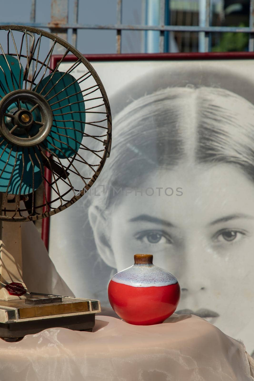 Bangkok, Thailand - Feb 06, 2021: Small red ceramic vases with old vintage fan on pink textured table cloth in front of Chinese poster movie frame at the balcony house. Home decor, Selective focus.