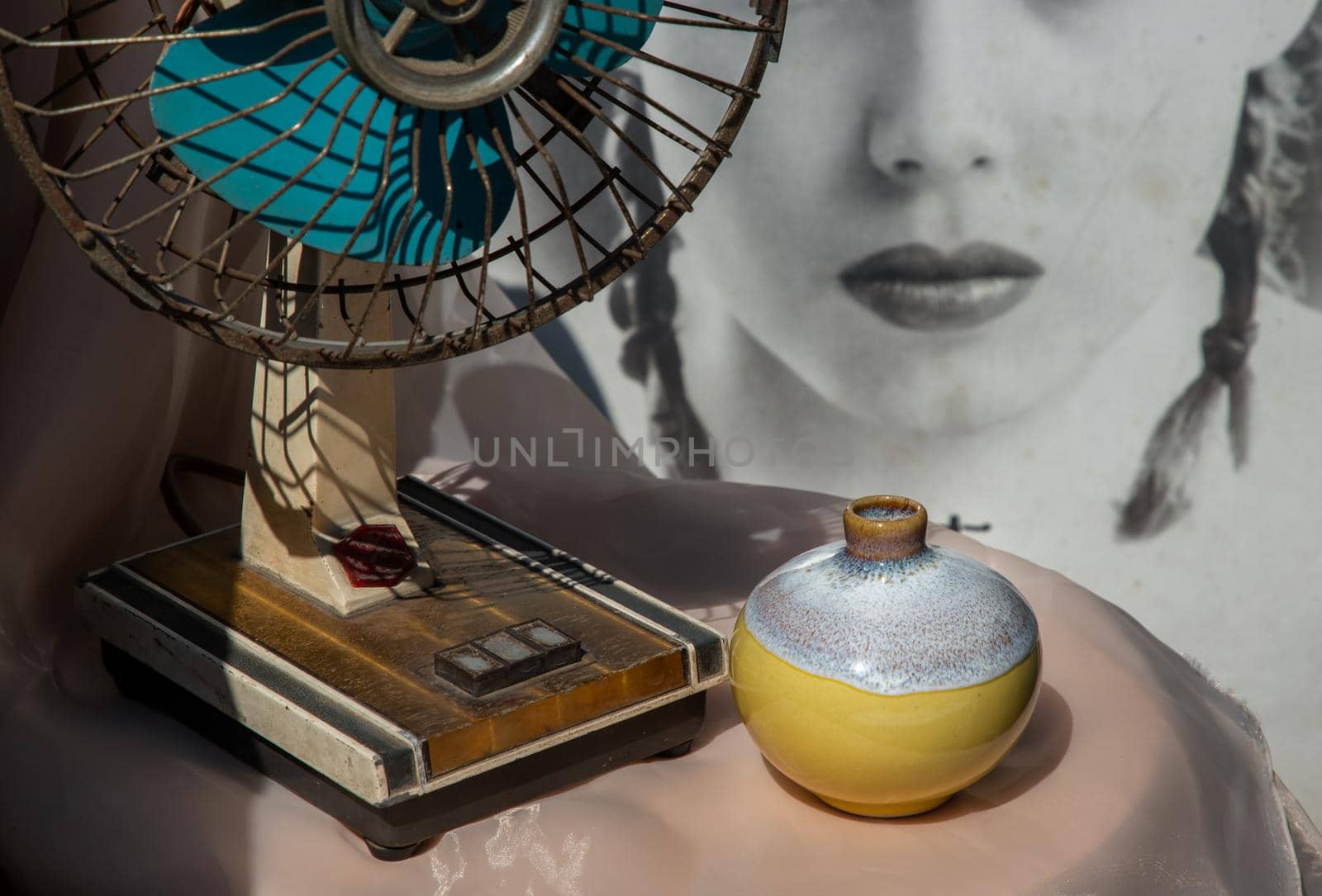 Bangkok, Thailand - Feb 06, 2021: Small yellow ceramic vases with old vintage fan on pink textured table cloth in front of Chinese poster movie frame. Home decor, Selective focus.