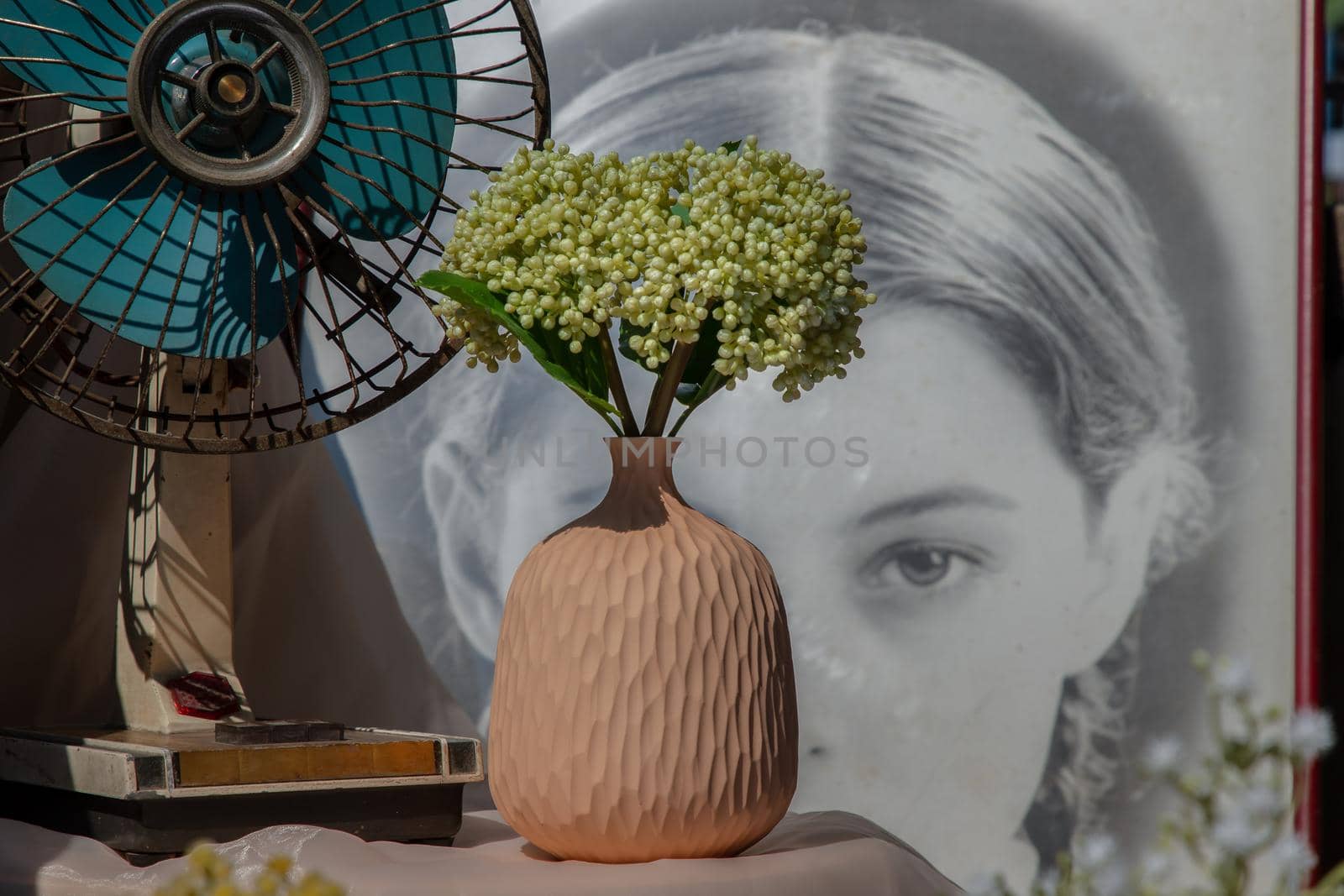 Bangkok, Thailand - Feb 06, 2021: Bouquet of green flowers in Handmade ceramic vase and old vintage fan on pink textured table cloth in front of Classic chinese poster movie frame. Home decor, Selective focus.