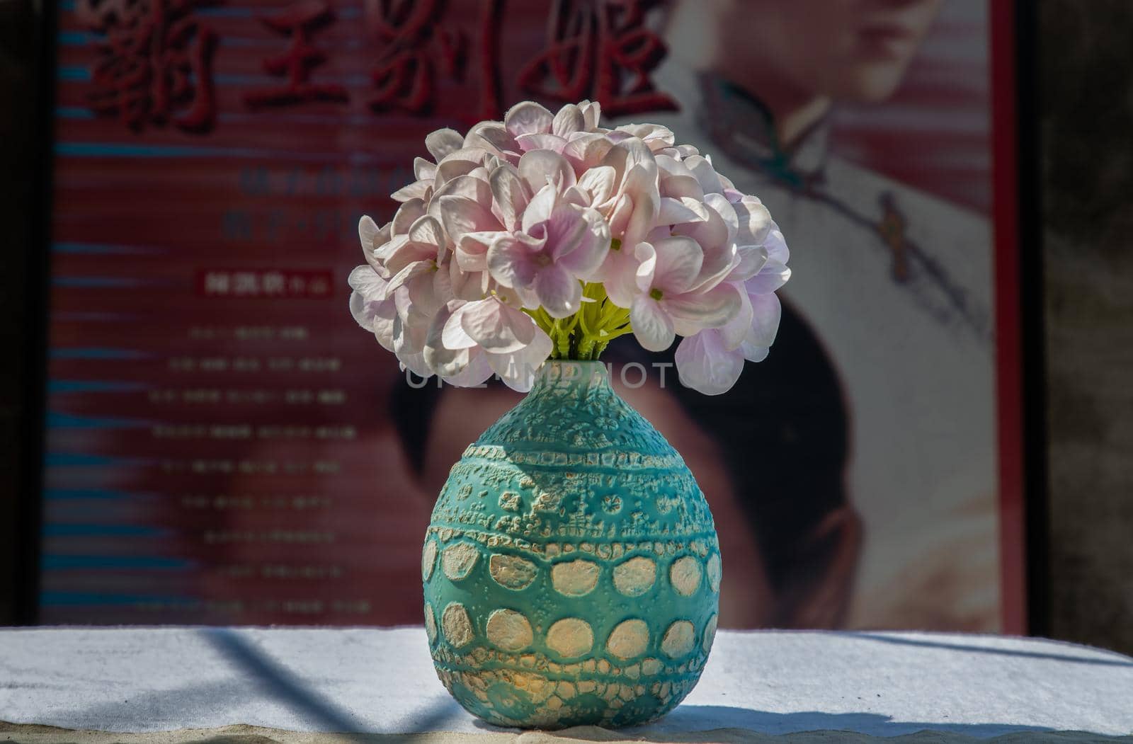 Bangkok, Thailand - Feb 06, 2021: Bouquet of purple flowers in Blue handmade ceramic vase on white textured table cloth in front of Classic chinese poster movie frame. Home decor, No focus, specifically.