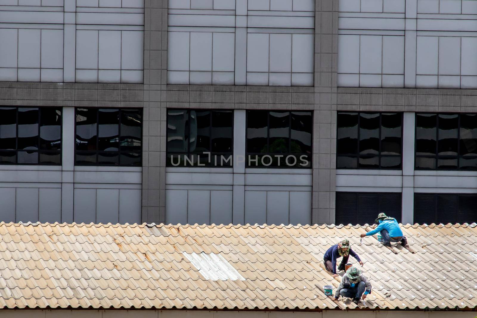 Bangkok, Thailand - 13 Jun 2020 : Three handyman workers repairing tiles on the damaged factory roof.