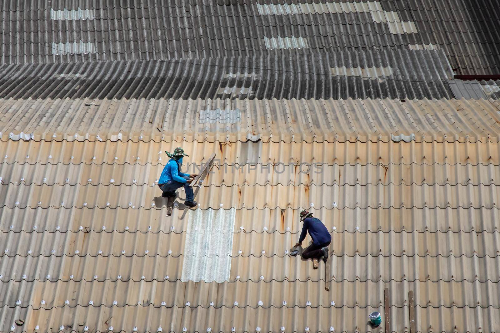 Bangkok, Thailand - 13 Jun 2020 : Two handyman workers repairing tiles on the damaged factory roof.
