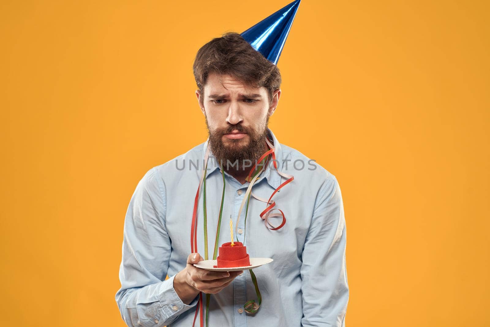 Cheerful man with a cake on a yellow background birthday holidays cap on his head by SHOTPRIME