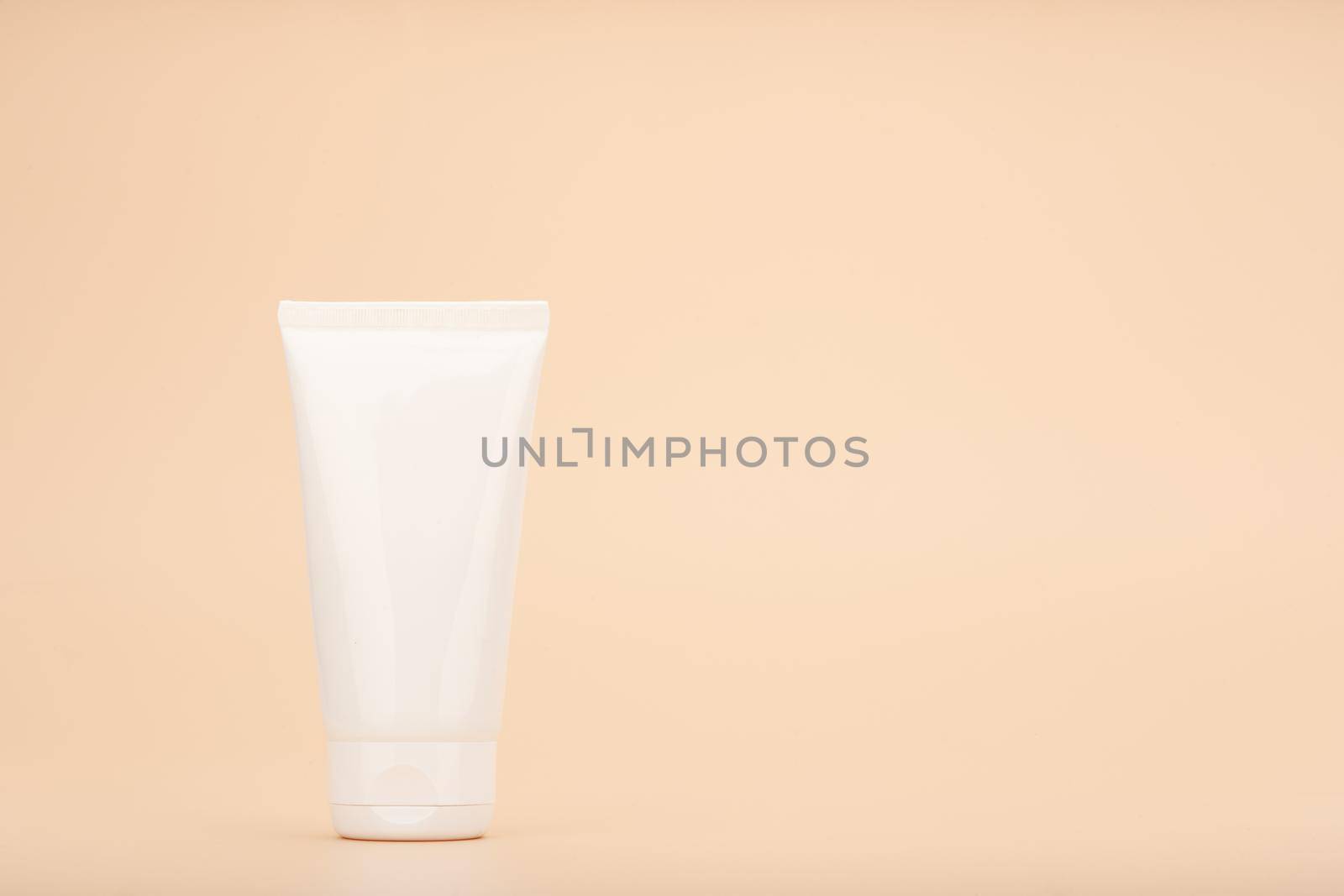 White cream tube against beige background with copy space. Concept of beauty products for skin care. Skin cream, mask scrub or exfoliation product