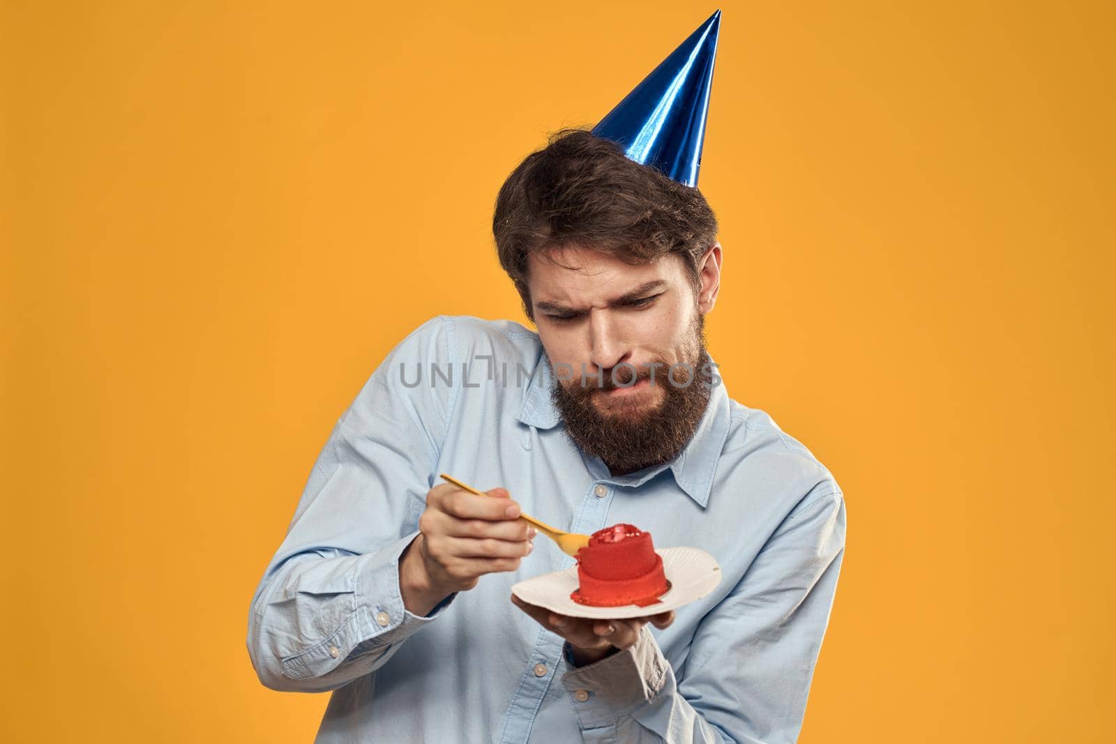 a man with a birthday cake in his hands and in a cap on a yellow background on his birthday. High quality photo