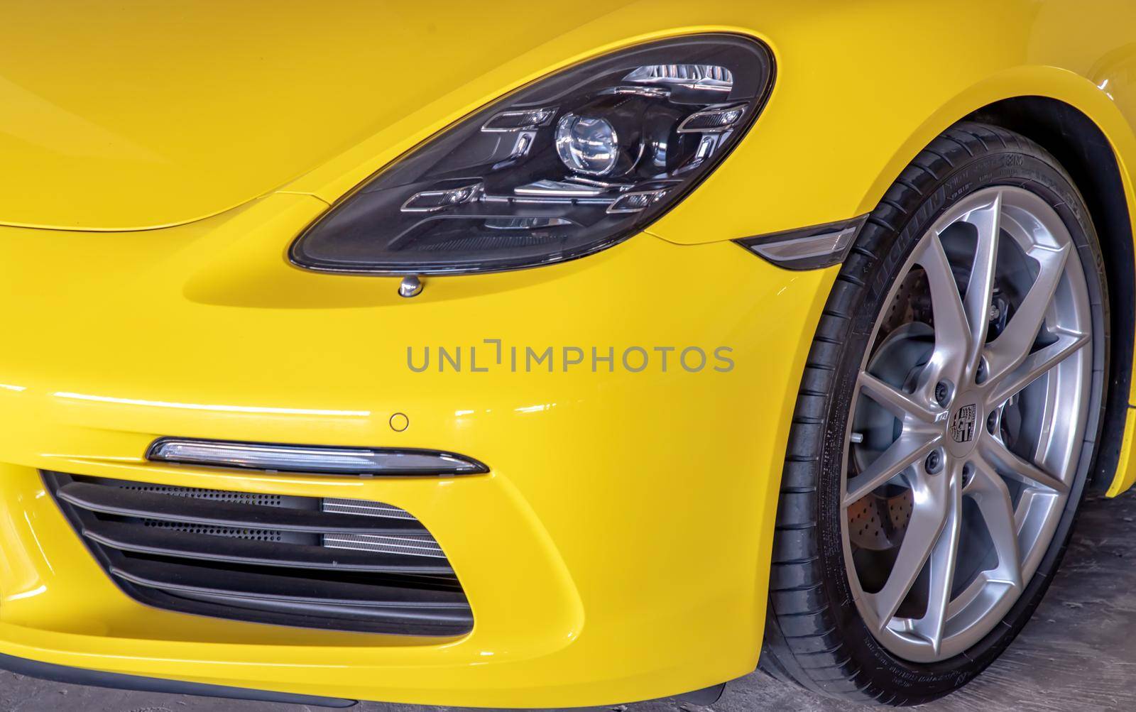 Bangkok, Thailand - 06 Jan 2021 : Close-up of Car Headlights and Car Wheel of Yellow Porsche Sports Car parked in the parking lot. Selective focus.