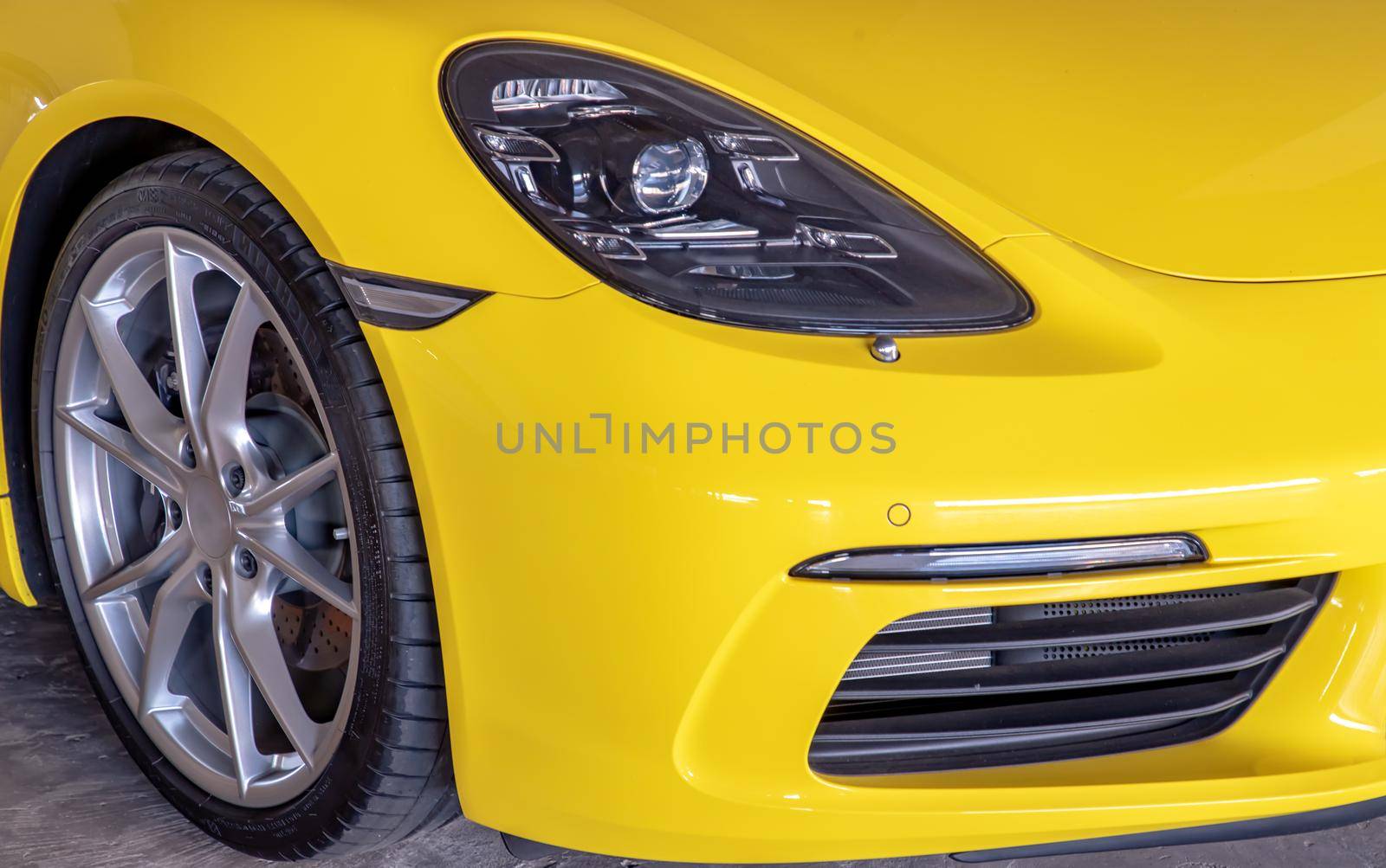 Bangkok, Thailand - 06 Jan 2021 : Close-up of Car Headlights and Car Wheel of Yellow Porsche Sports Car parked in the parking lot. Selective focus.