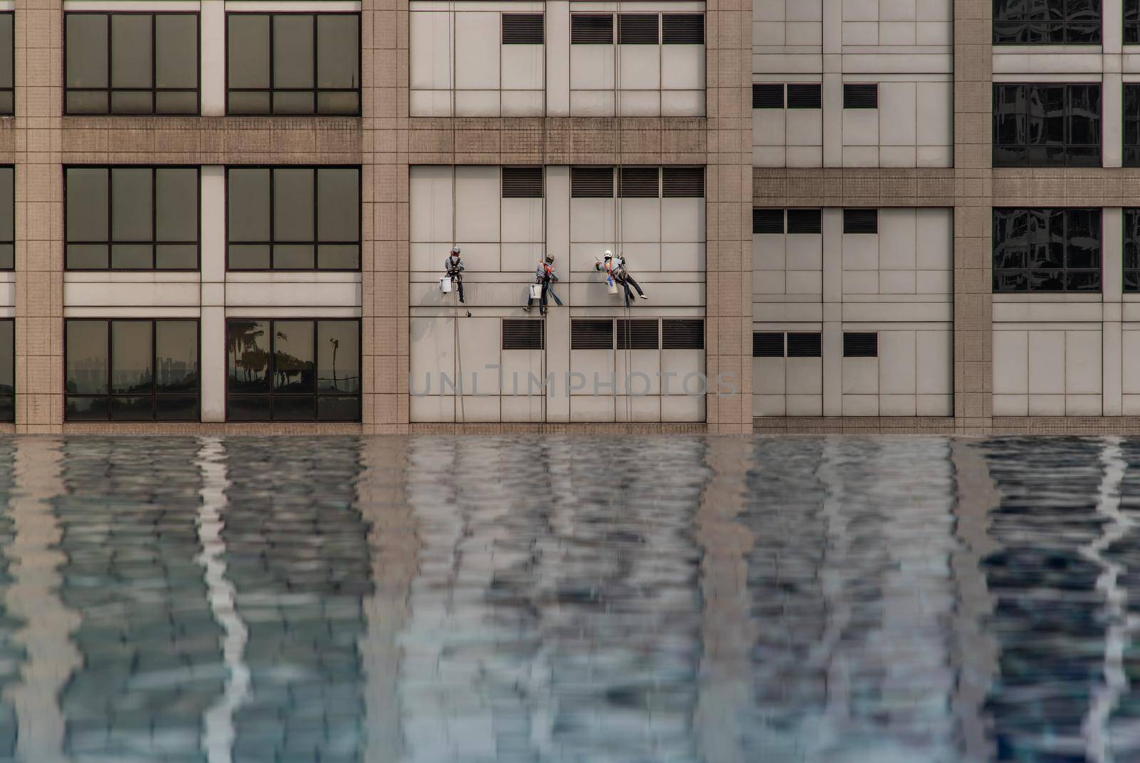 Group of workers cleaning windows service on high rise office building with reflection from swimming pool. Selective focus.
