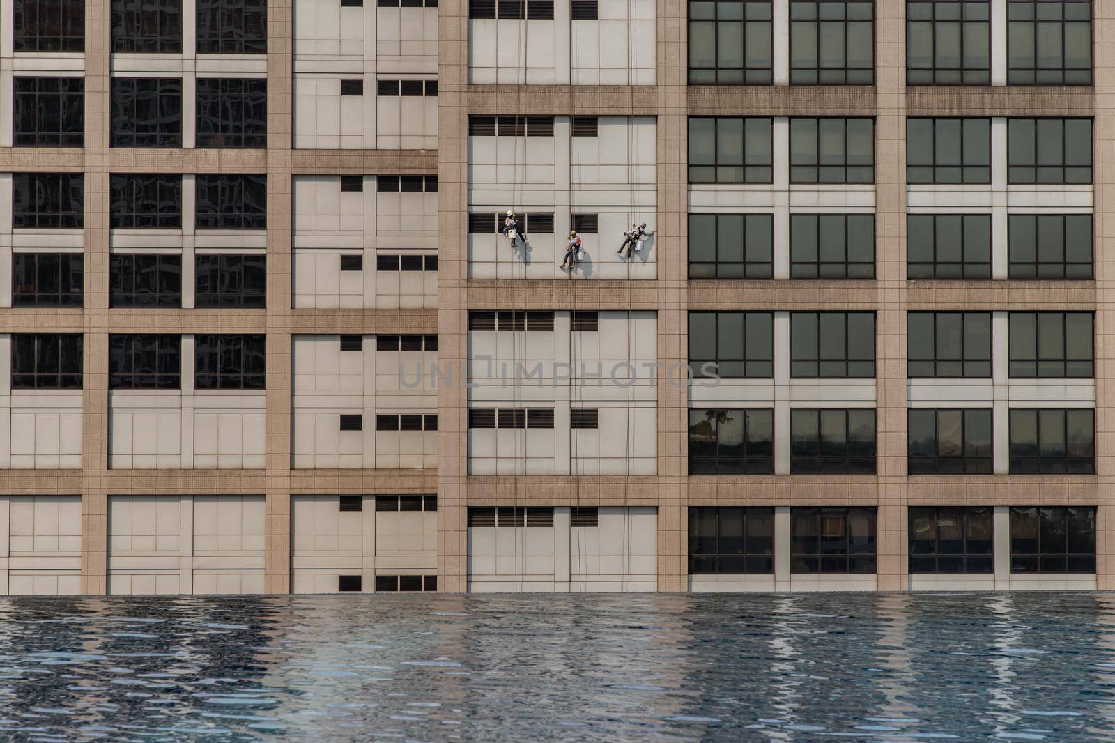 Group of workers cleaning windows service on high rise office building with reflection from swimming pool. Selective focus.