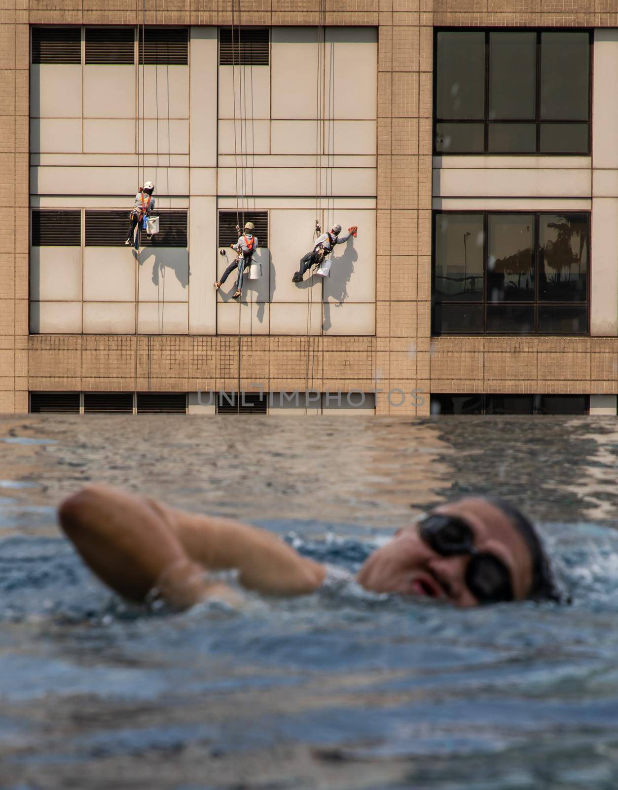 Group of workers cleaning windows service on high rise office building with reflection from swimming pool. Selective focus.